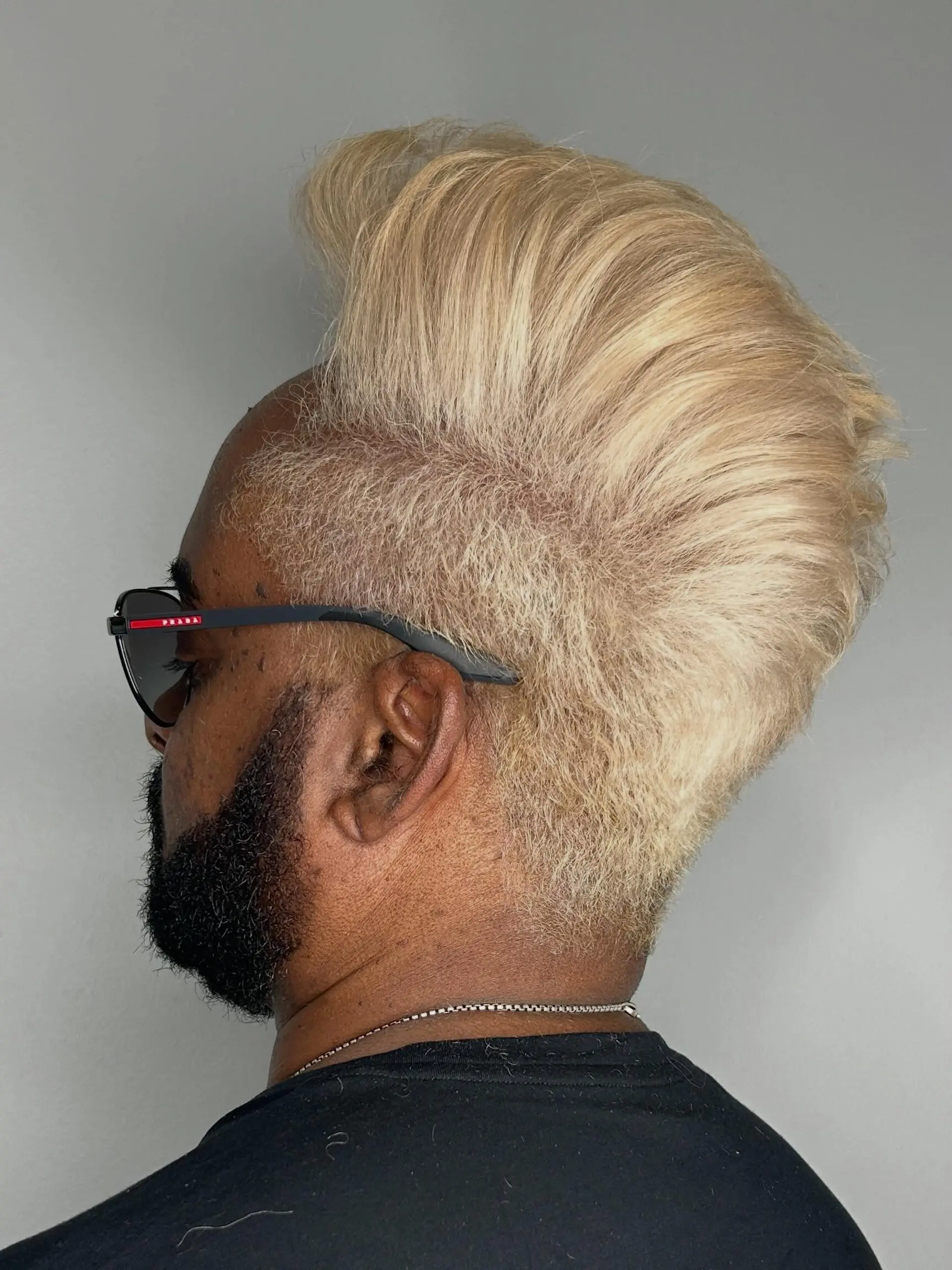 A bold platinum blonde voluminous faux hawk fade with high-swept texture on top and closely tapered sides contrasting with a dark beard. 1