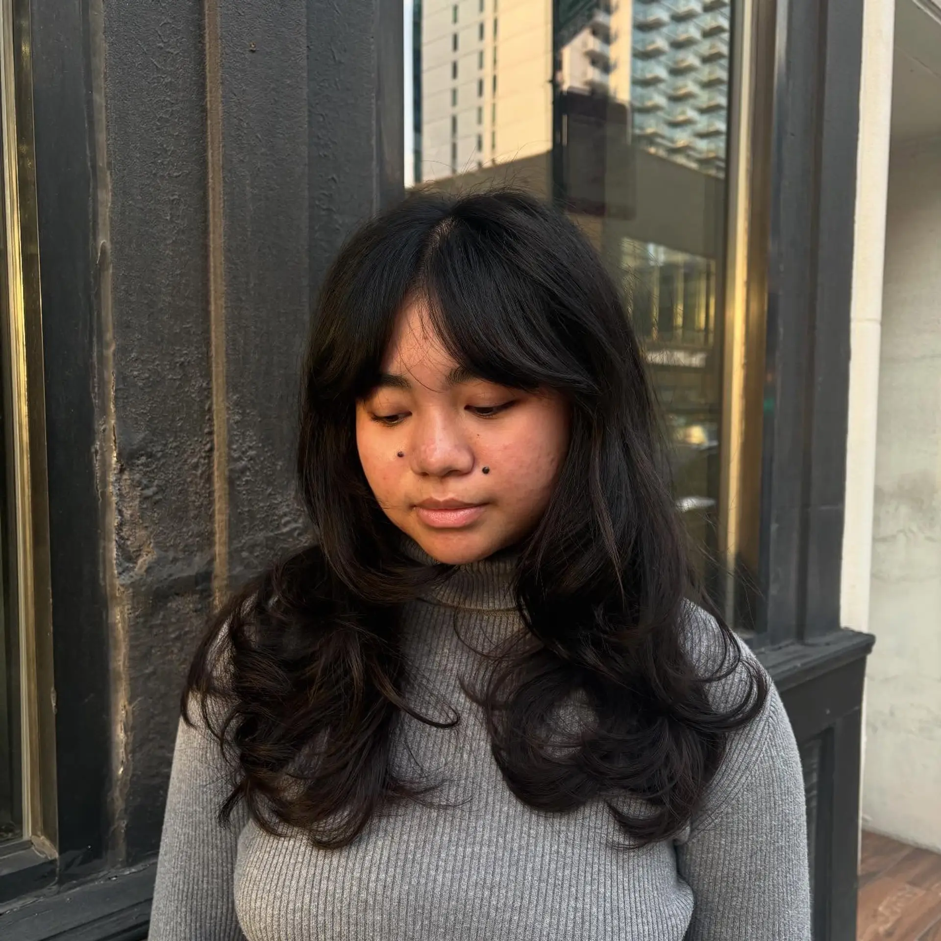Long dark layered haircut styled with feathered curtain bangs and soft, voluminous curled ends. 1