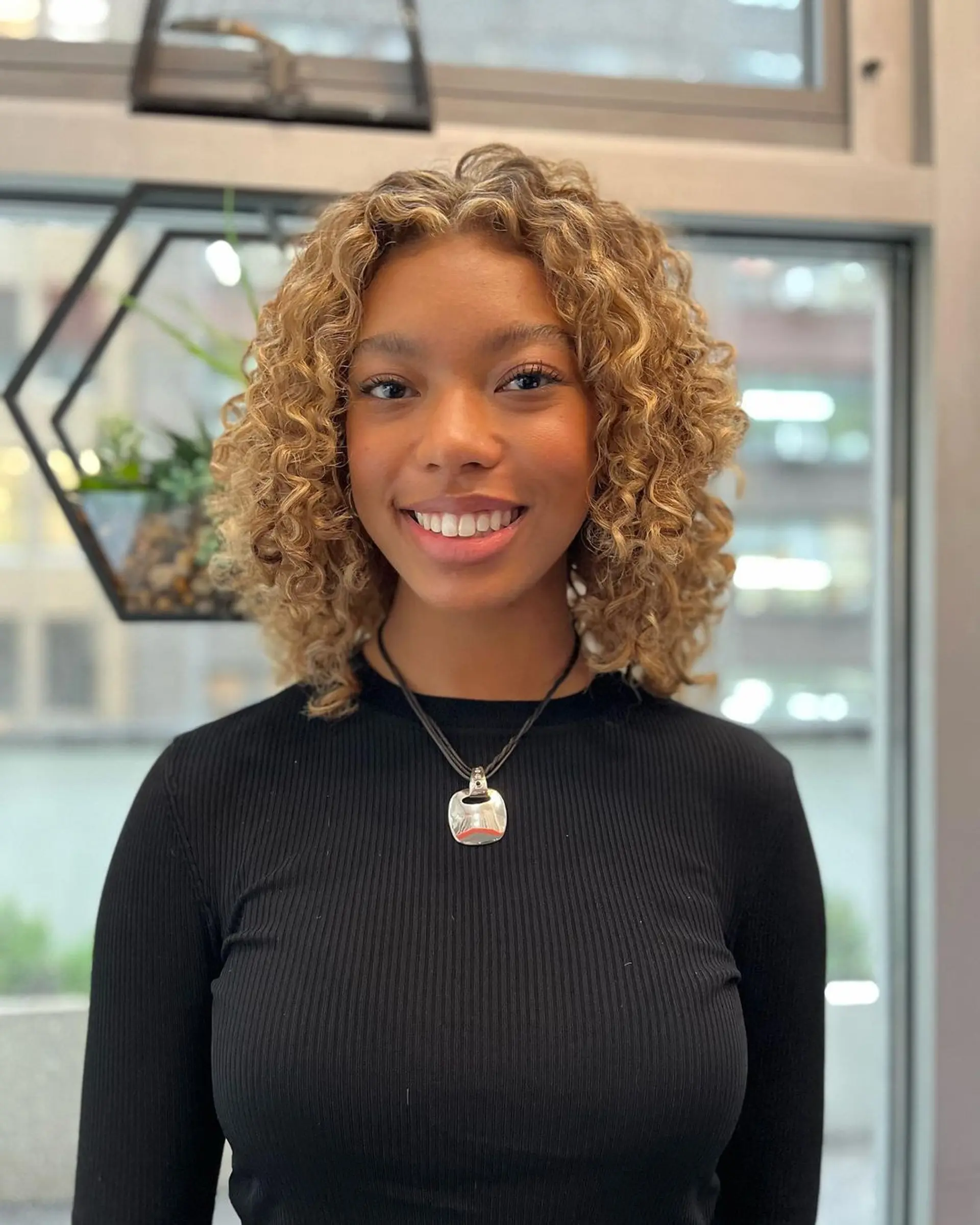 Medium-length curly hairstyle with honey blonde and golden brown hues. Natural curls form bouncy, voluminous ringlets with highlights, framing the face beautifully. 1