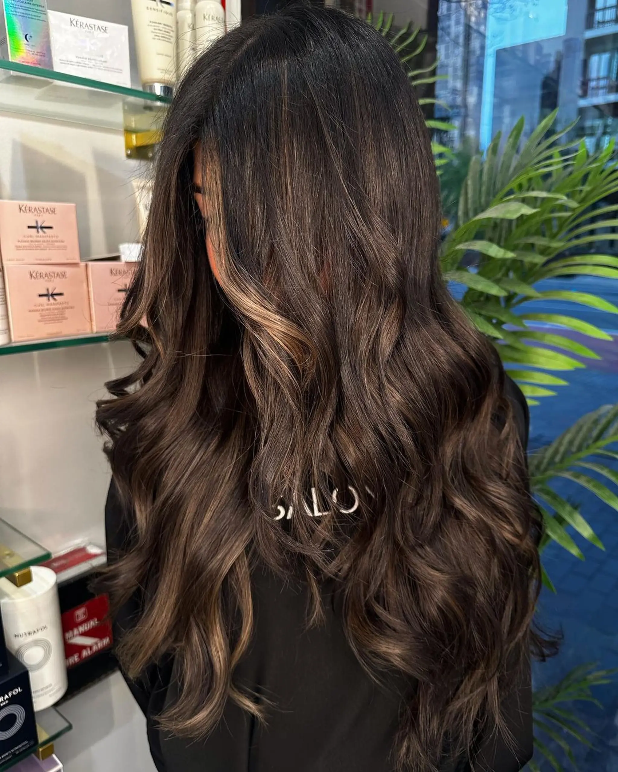 A long, wavy hairstyle with a dark brown base and caramel balayage highlights. This style features loose waves, a layered cut, and face-framing streaks.