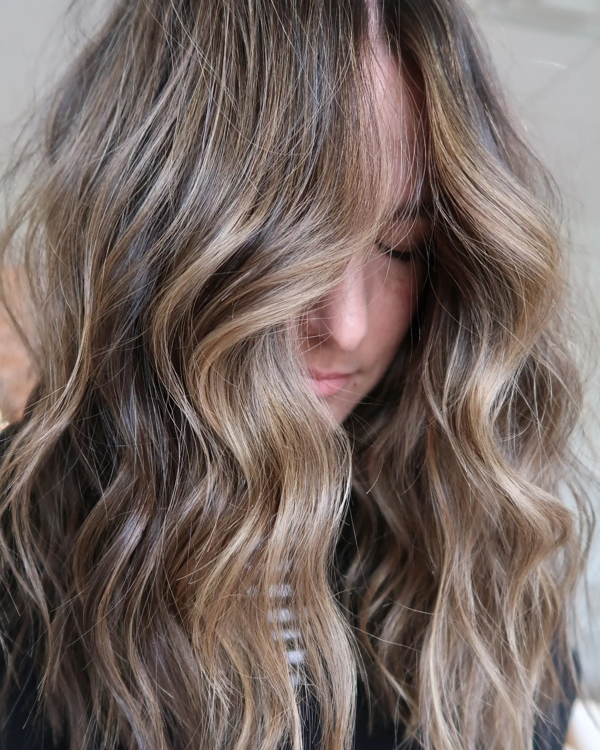 Long loose beach waves featuring a seamless dimensional balayage with blended blonde highlights over a neutral brunette base. 1
