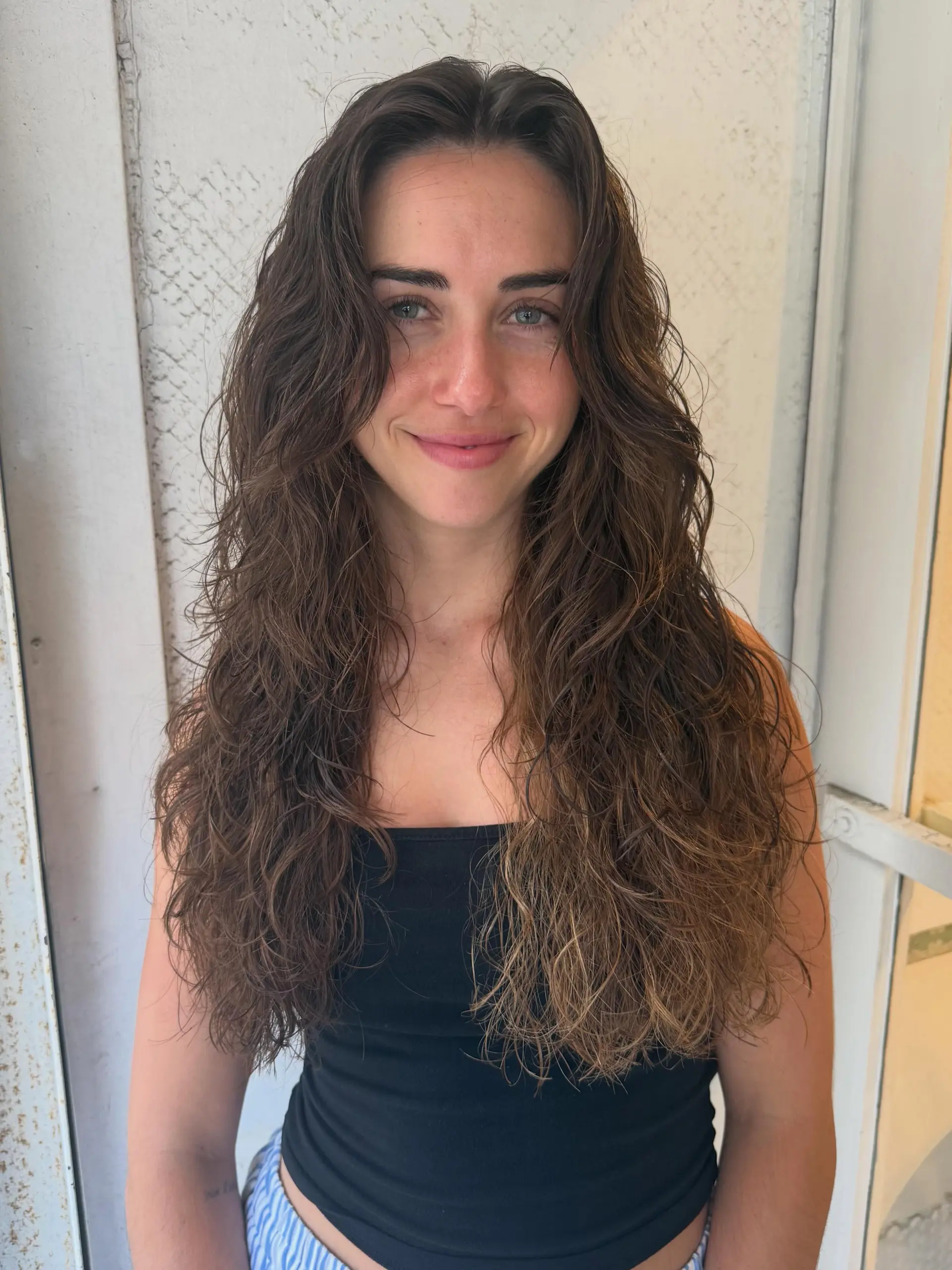 Long layered cut on naturally wavy, brunette hair with soft dimension and texture. 1