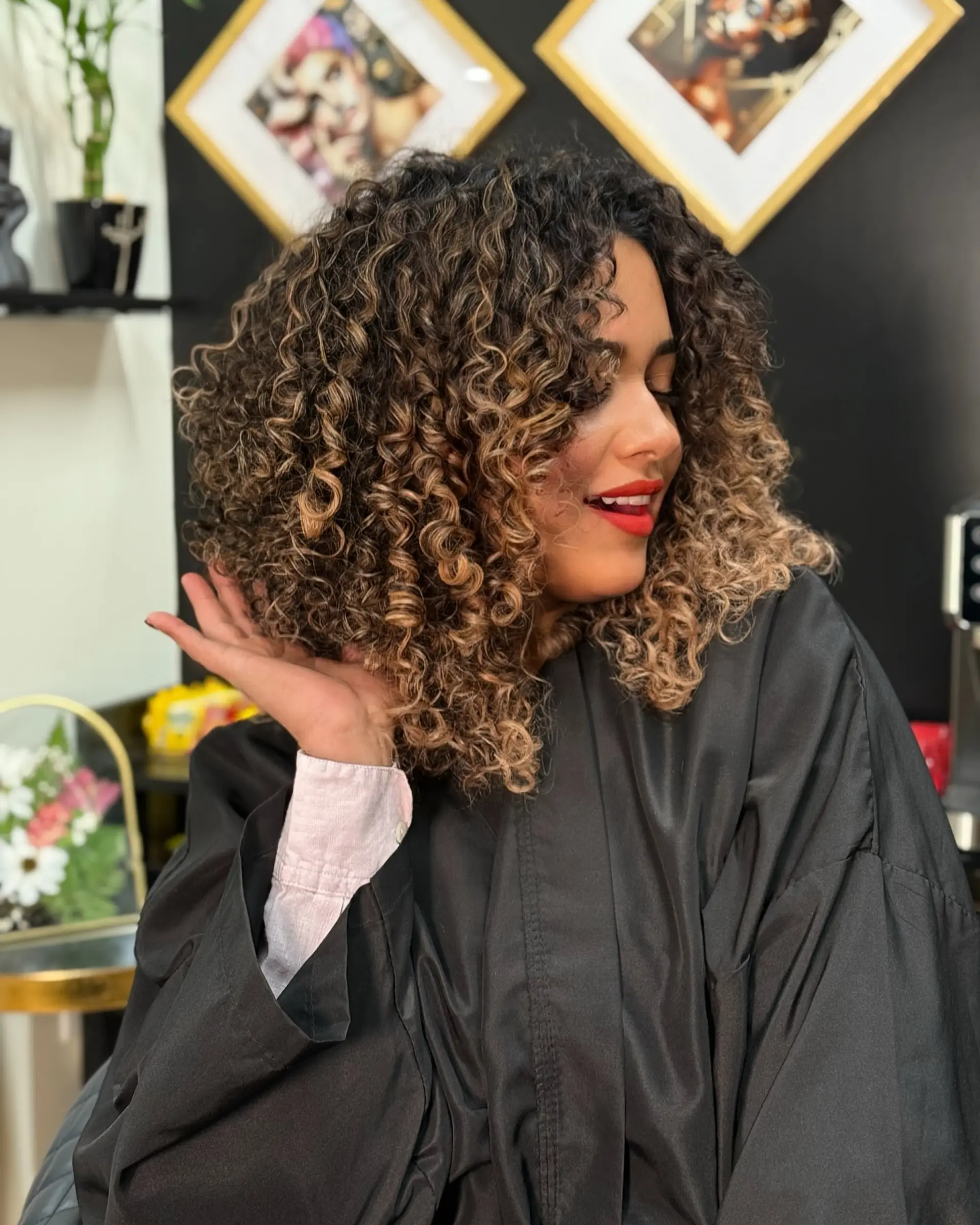 Shoulder-length, voluminous curly cut styled with tight, well-defined ringlets and caramel blonde highlights. 1