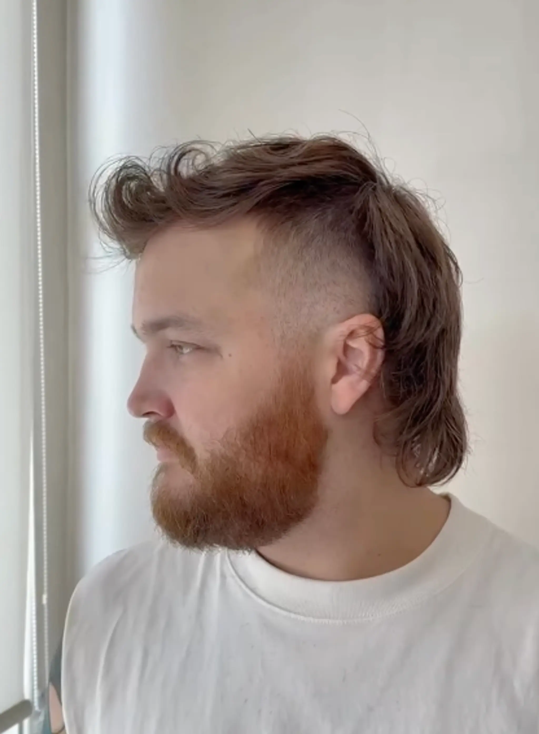 A modern mullet with a wavy texture, featuring an undercut fade and textured top. The medium-length hair sweeps back to neck-length layers, blending retro style with a contemporary finish.