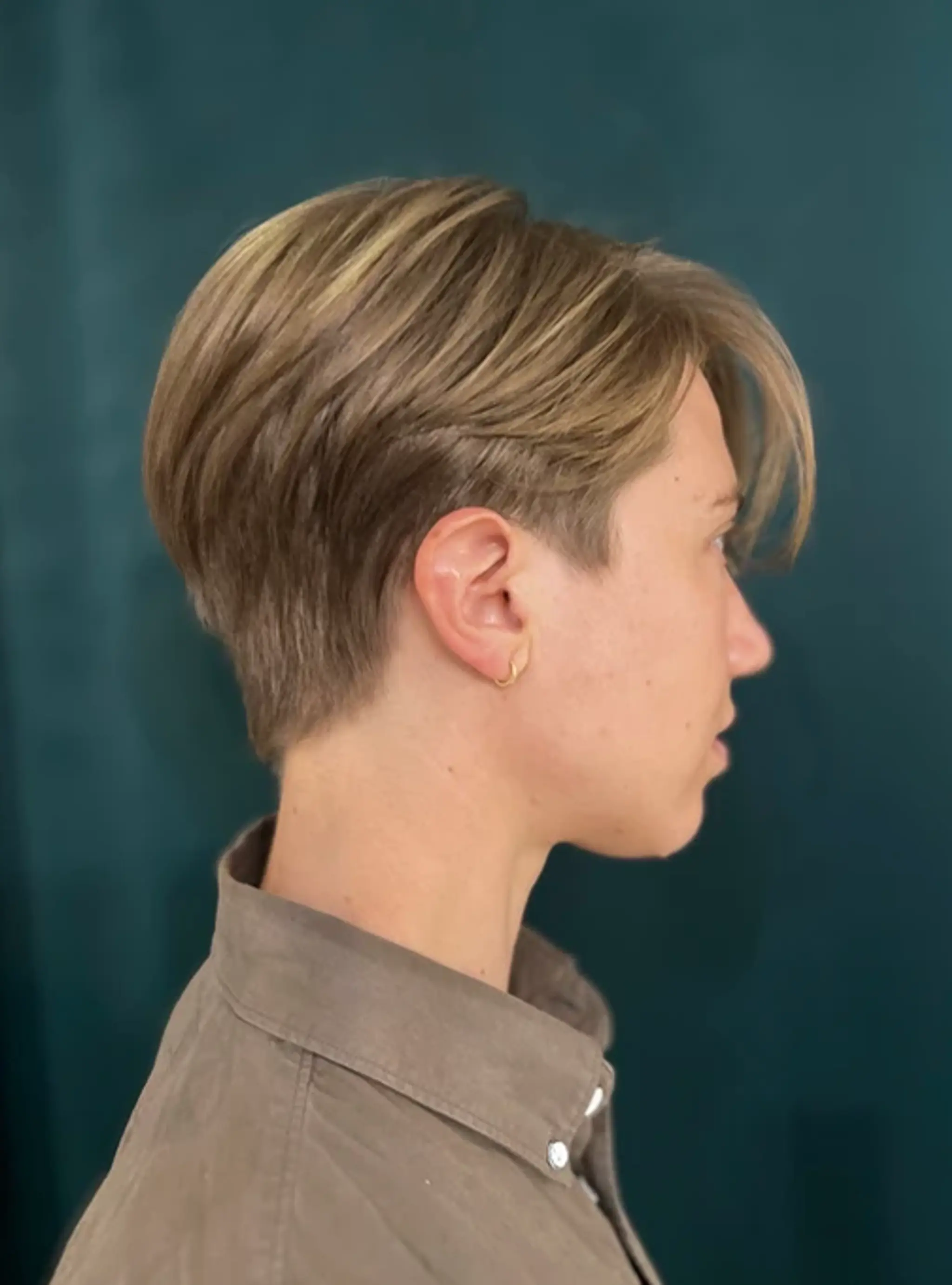 A sleek pixie cut with straight, golden blonde hair and ash blonde tones. The style includes a cropped back and sides with longer top layers and a side-swept fringe for added elegance.