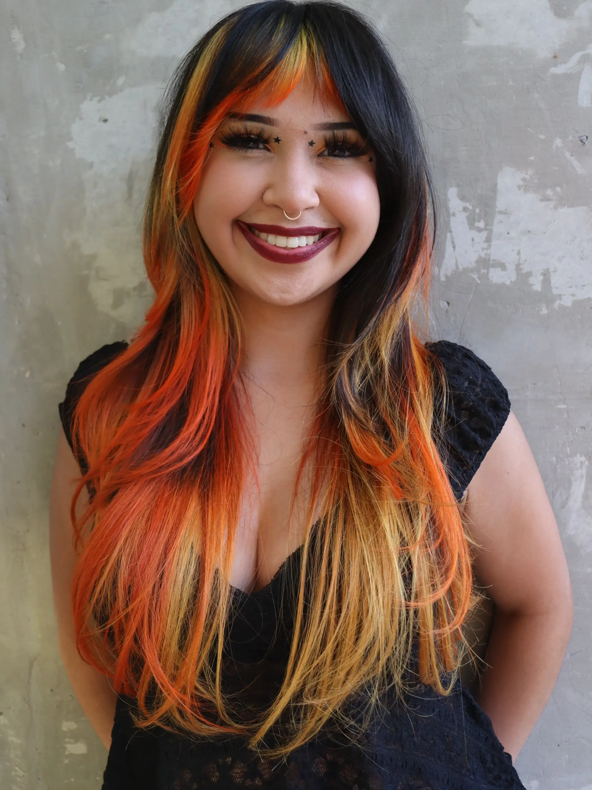 Long layered dark hair featuring vibrant fire-toned orange and yellow highlights framing the face and coloring the textured fringe. 1