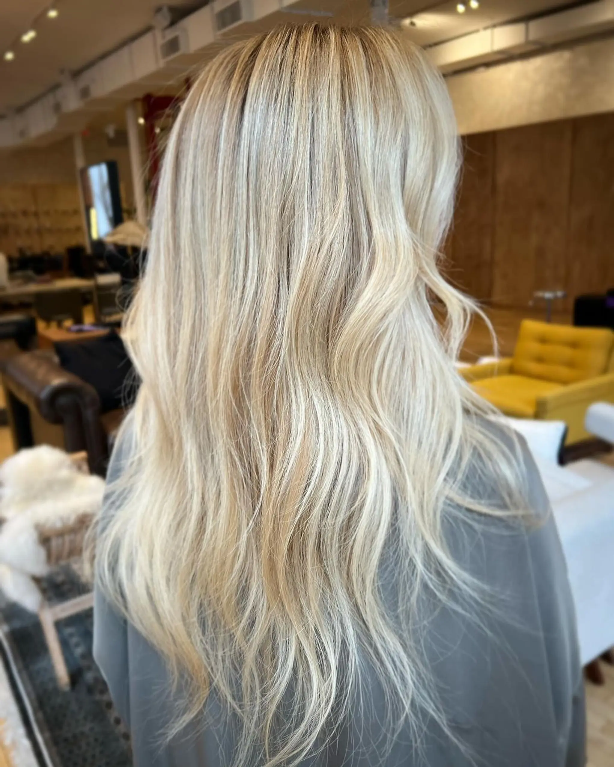 This hairstyle features long, blonde, wavy hair with soft, layered waves that create a natural, shiny appearance.