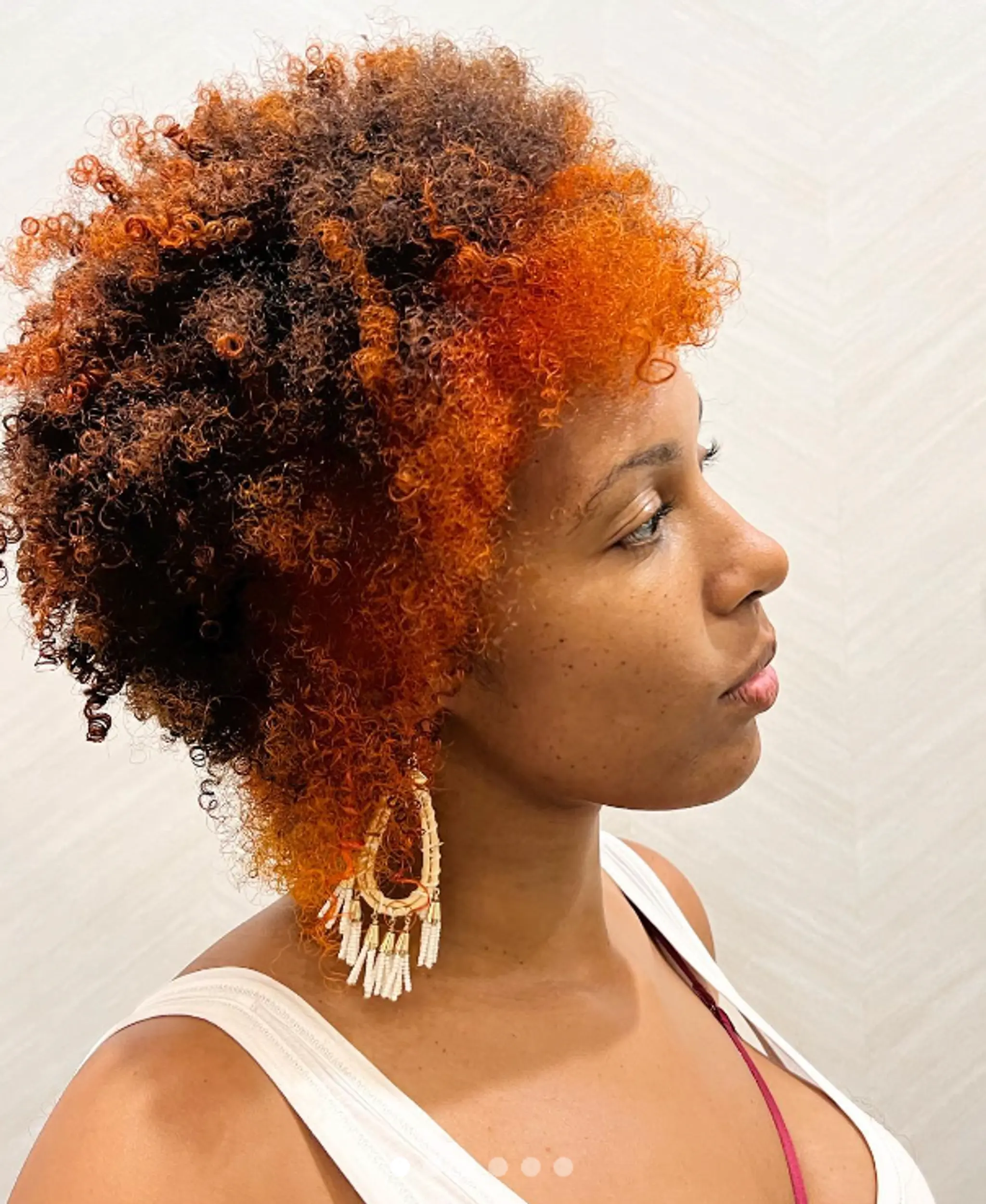 A short, curly afro with vibrant orange tips blending into dark brown and black roots. Featuring curly bangs and a voluminous, layered look.

Color by @simabeautynyc
Cut and style by @juliamannino_hair
 1
