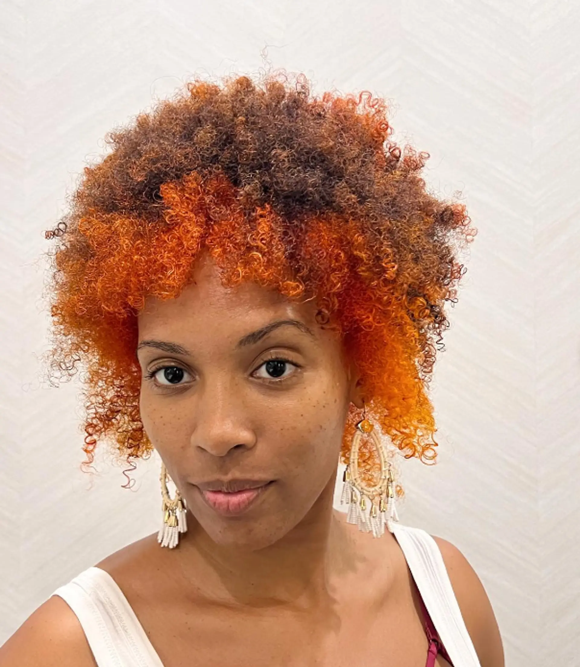 A short, curly afro with vibrant orange tips blending into dark brown and black roots. Featuring curly bangs and a voluminous, layered look.

Color by @simabeautynyc
Cut and style by @juliamannino_hair
 2