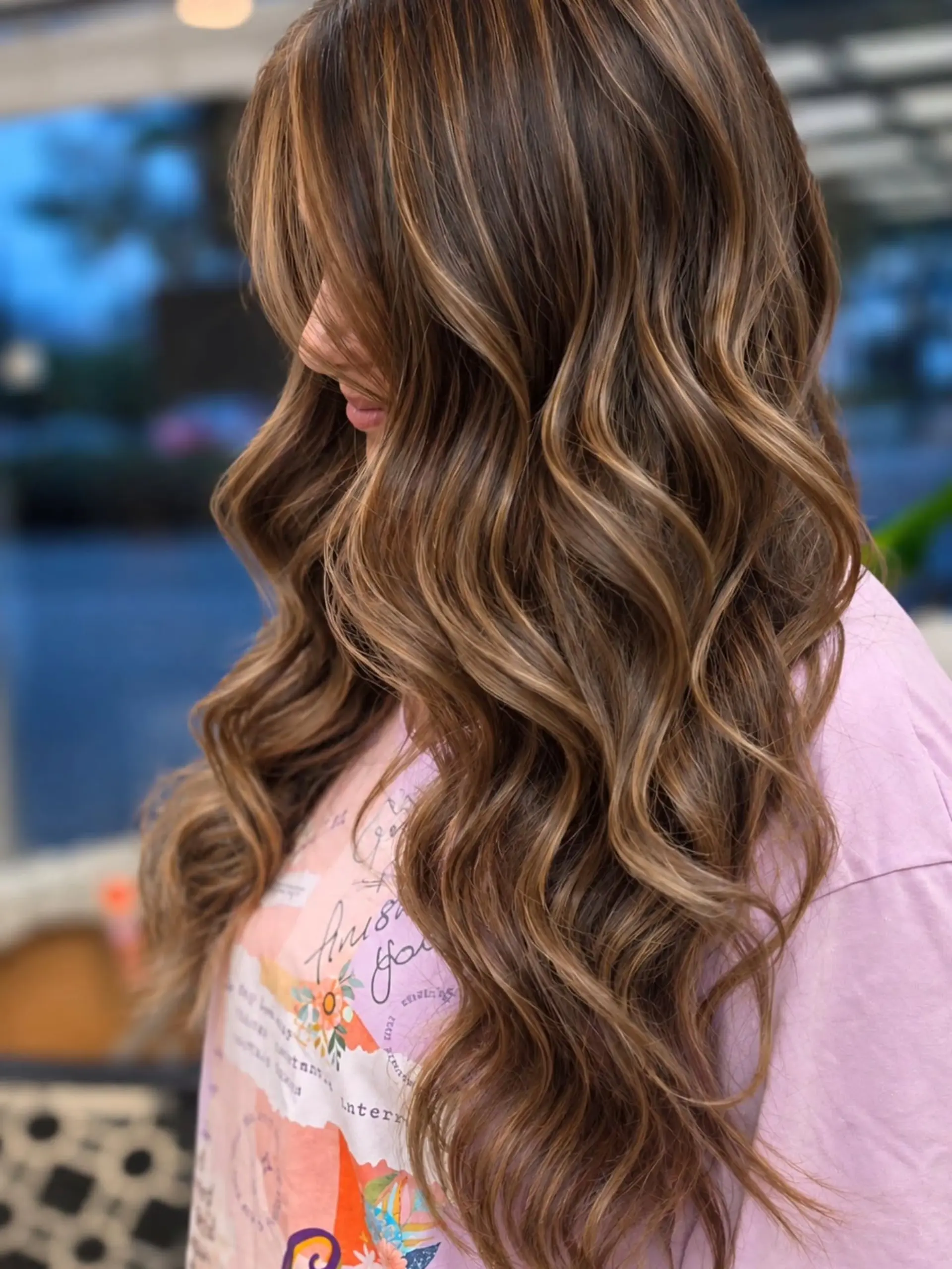 Long dark brown hair enhanced with warm caramel balayage highlights and styled in soft loose waves. 1