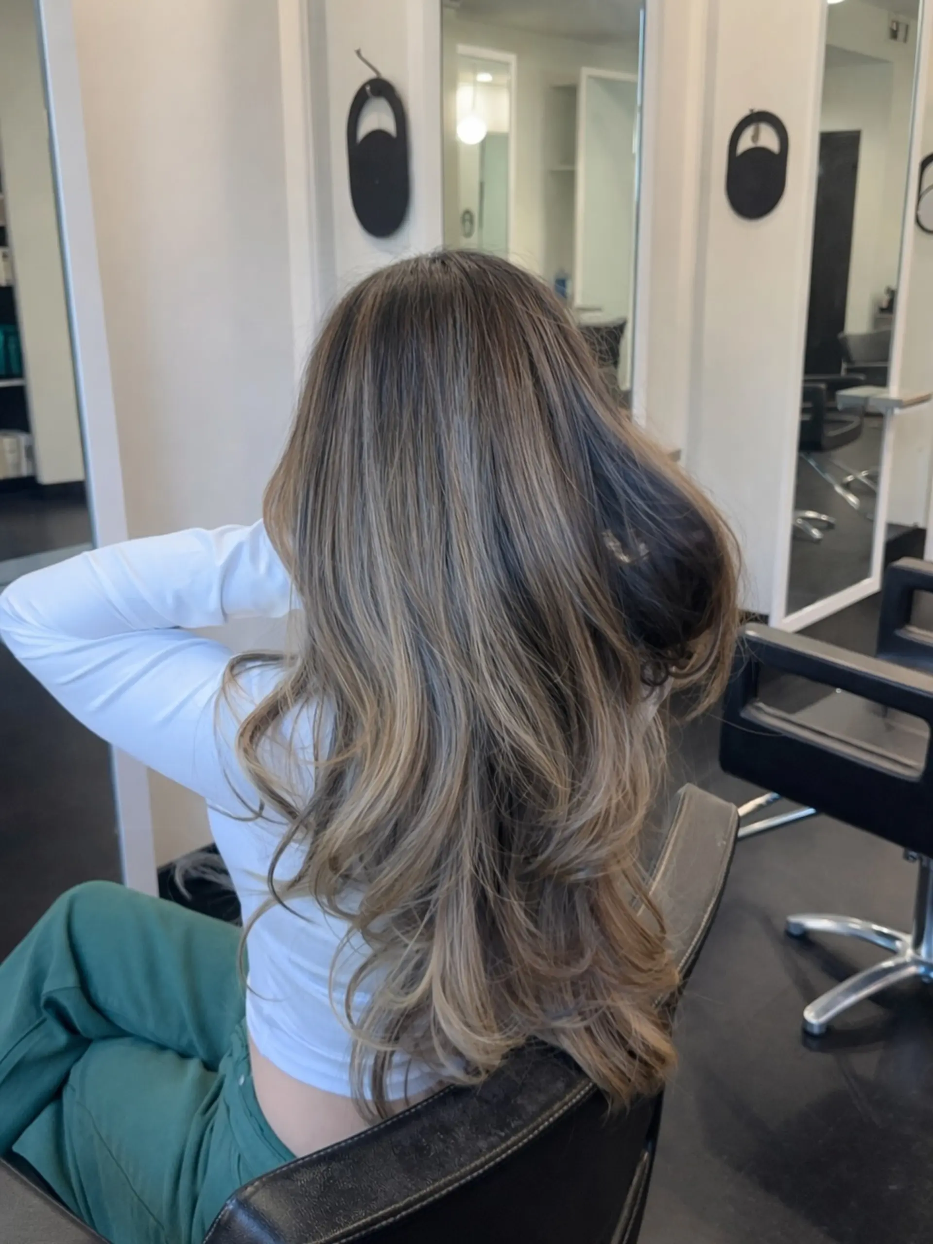 Long flowing hair styled in voluminous soft waves, showcasing a seamless dimensional bronde balayage with face-framing and blended layers. 1