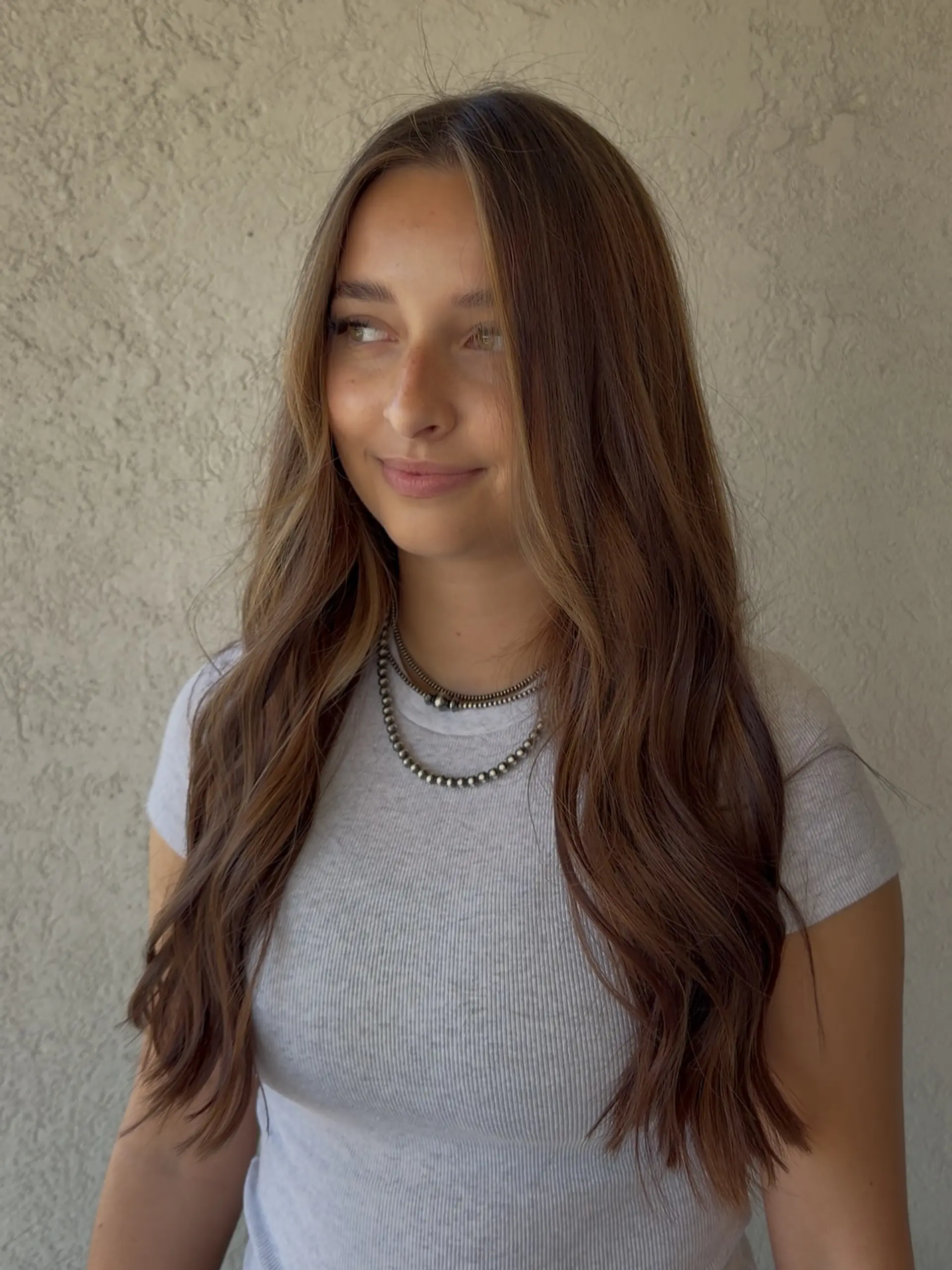 Long, dimensional brunette hair styled in loose, natural waves with soft face-framing dimension. 1