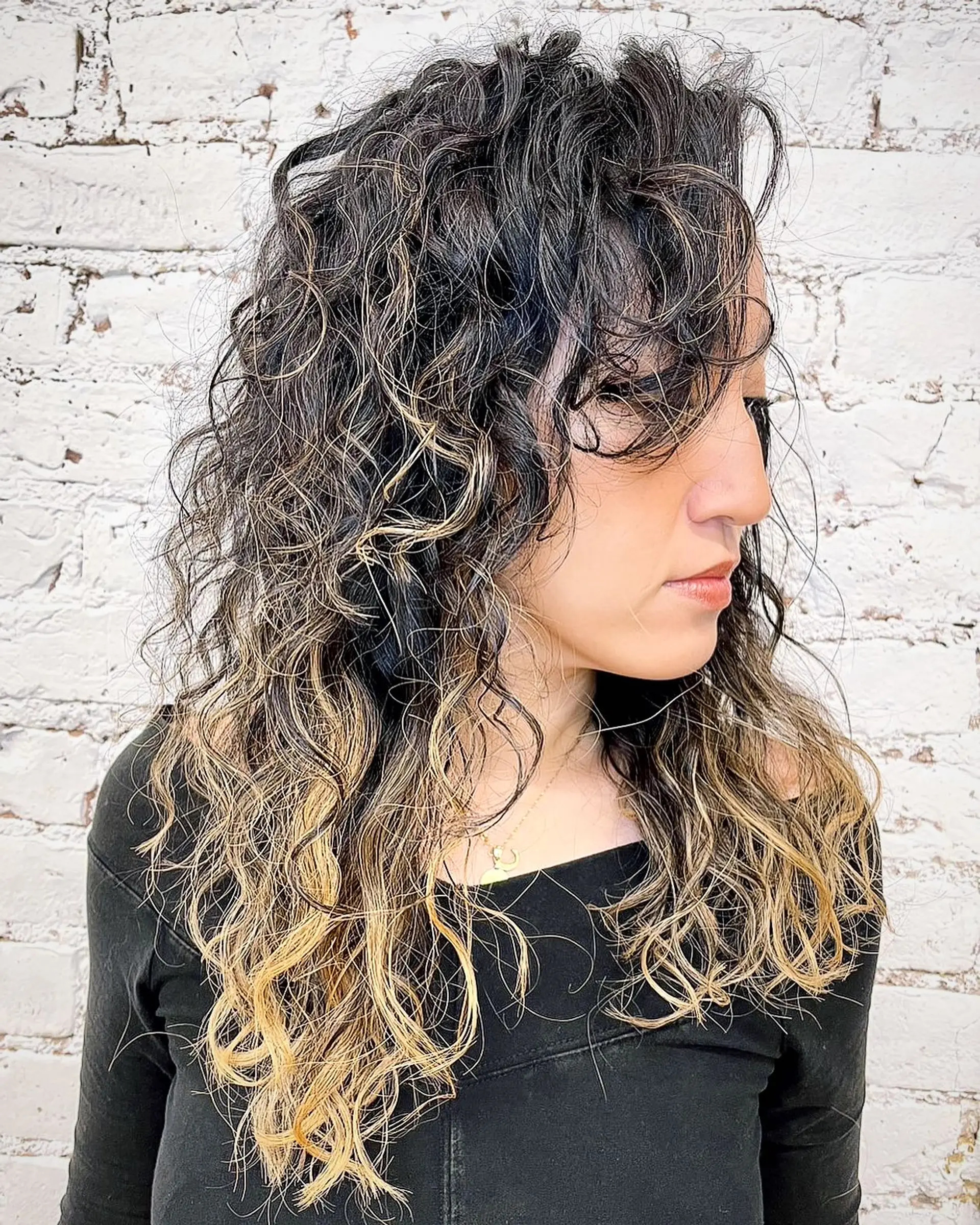Long naturally curly hair with soft face-framing fringe and warm honey blonde balayage ombre ends. 1