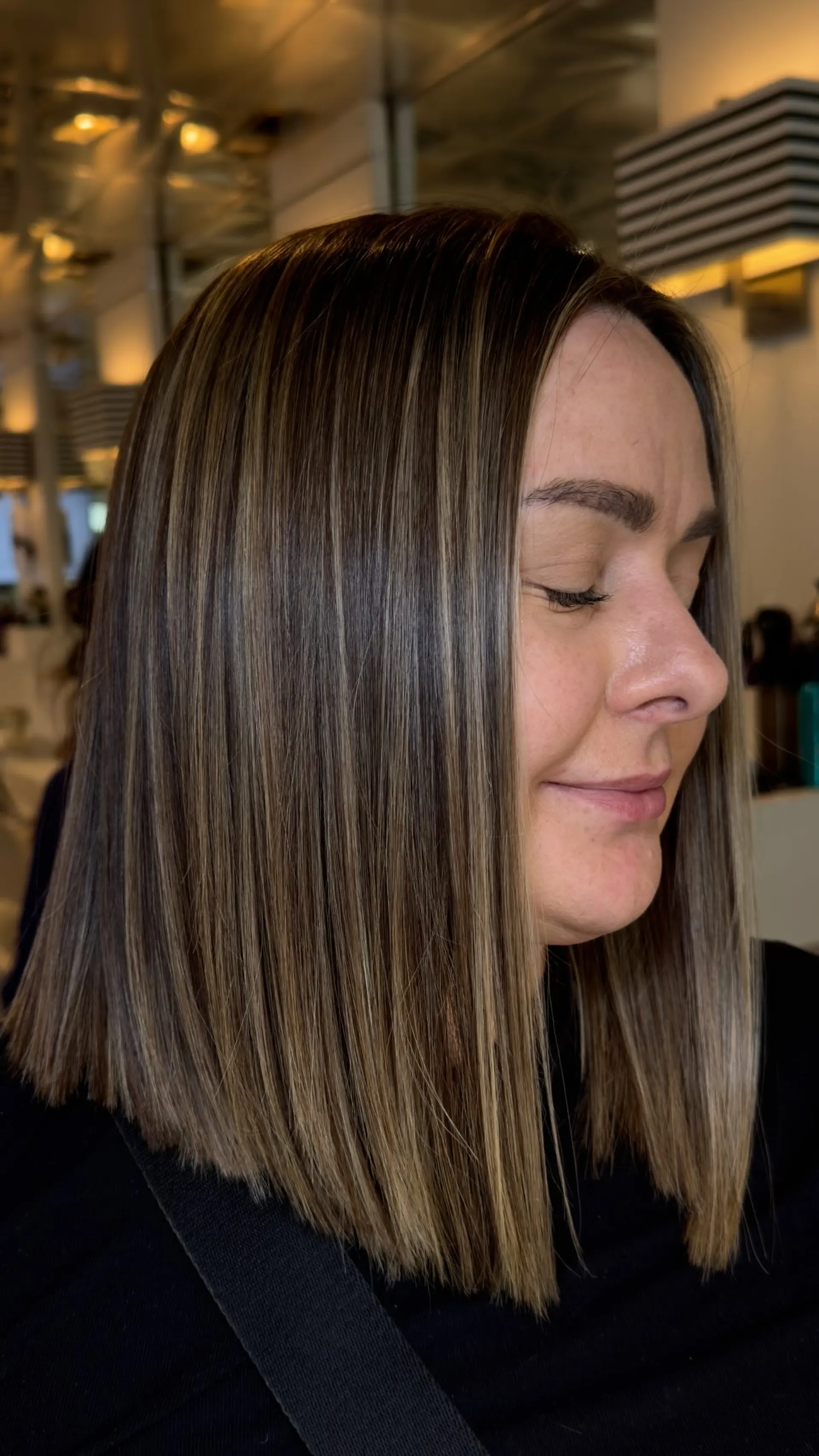 A blunt, shoulder-grazing long bob styled bone-straight with seamless, finely woven caramel and beige-blonde highlights over a rich brown base. 1