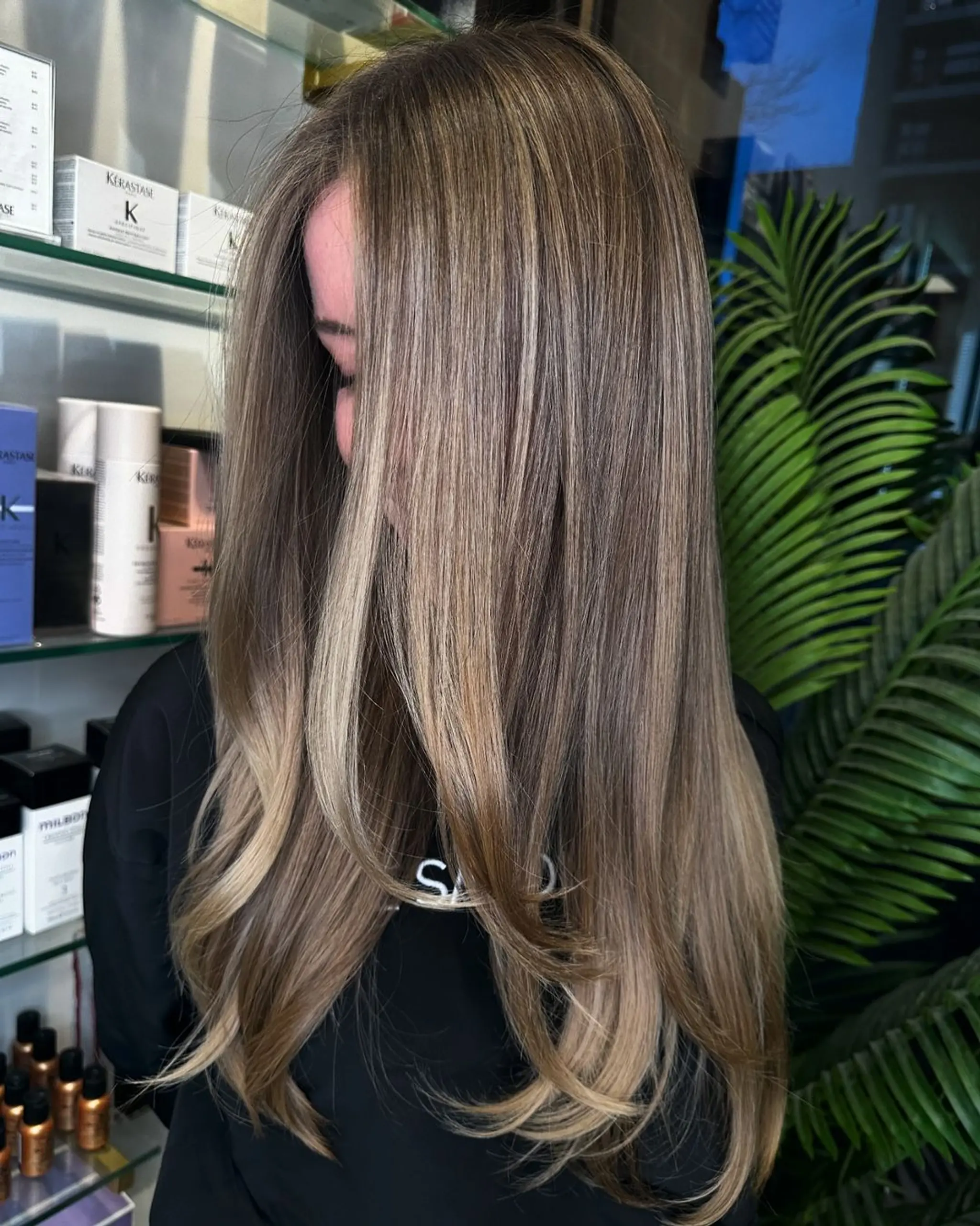 Long, wavy hair with balayage blending blonde and brown tones. Glossy finish with face-framing layers.