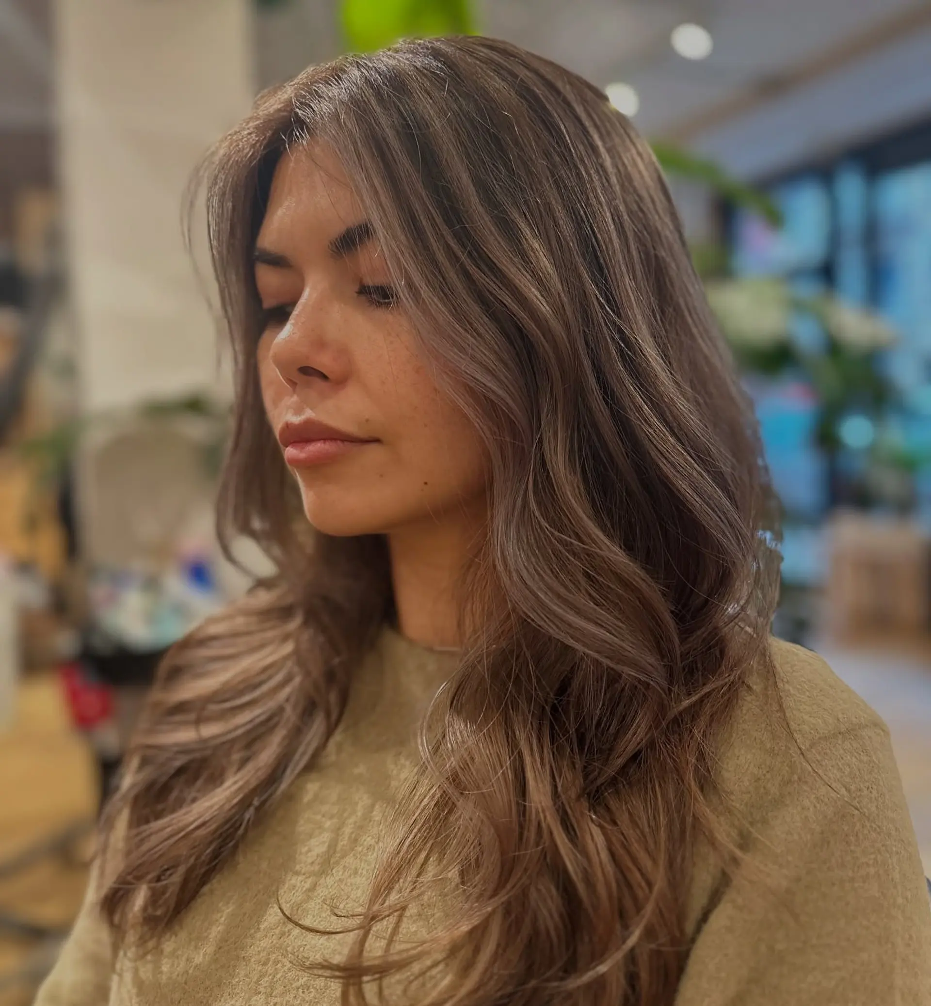 A cool-toned ash brown balayage styled with voluminous, soft cascading waves and face-framing layers. 1