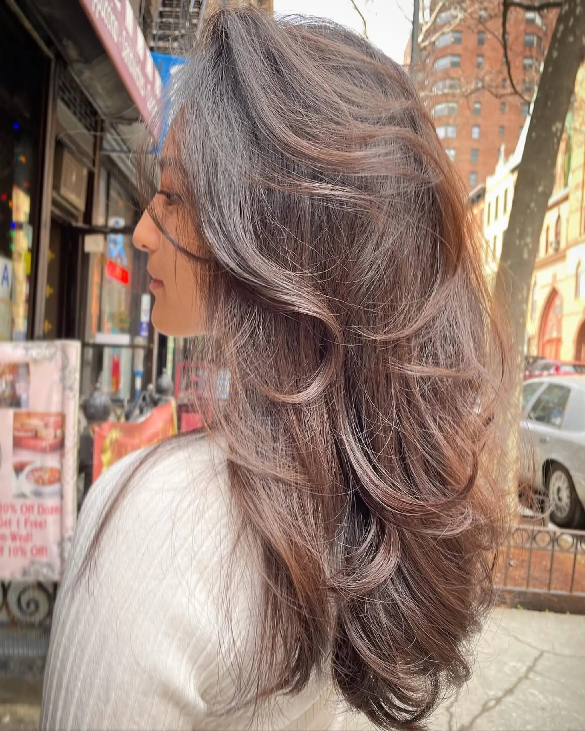 A long, wavy hairstyle with natural brown color and subtle highlights, featuring layered and textured strands for a voluminous, breezy look.