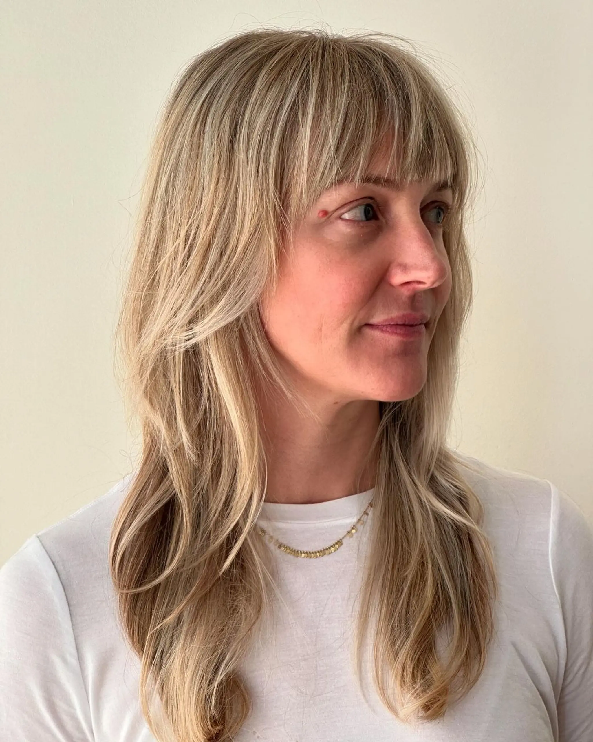 A long, wavy, sun-kissed blonde hairstyle with feathered bangs and natural layers.
