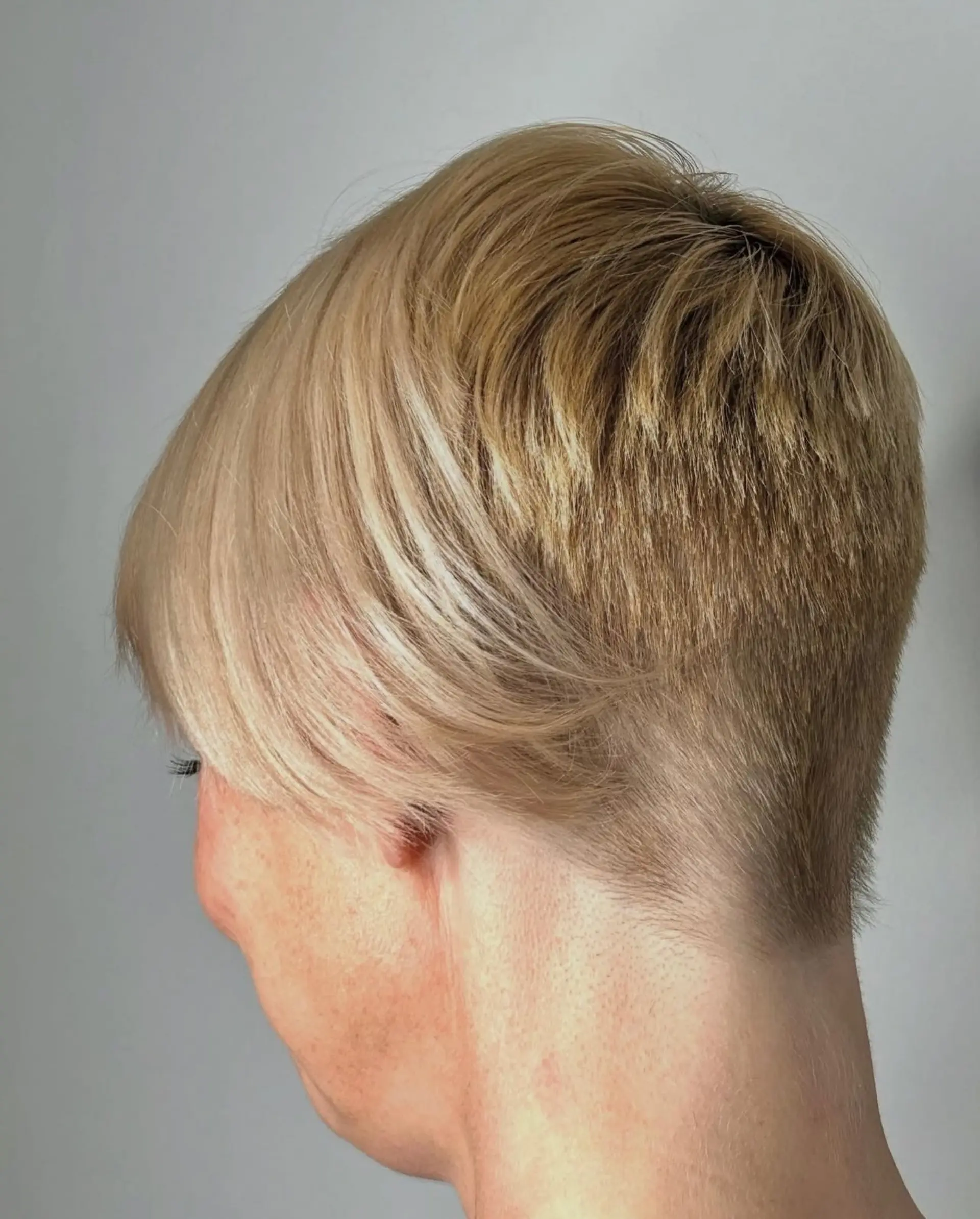 A sleek blonde pixie haircut featuring a closely tapered nape and soft, side-swept layers on the crown. 1