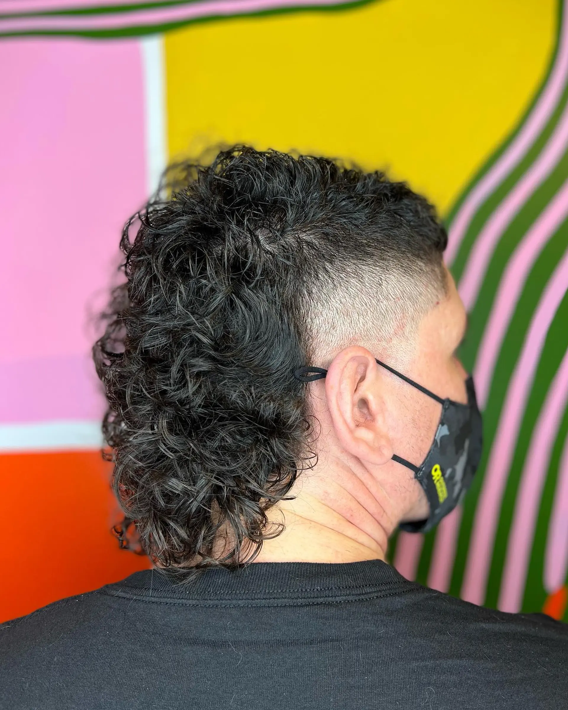 A modern curly mullet featuring a clean skin fade on the sides and textured, defined curls through the top and back. 1