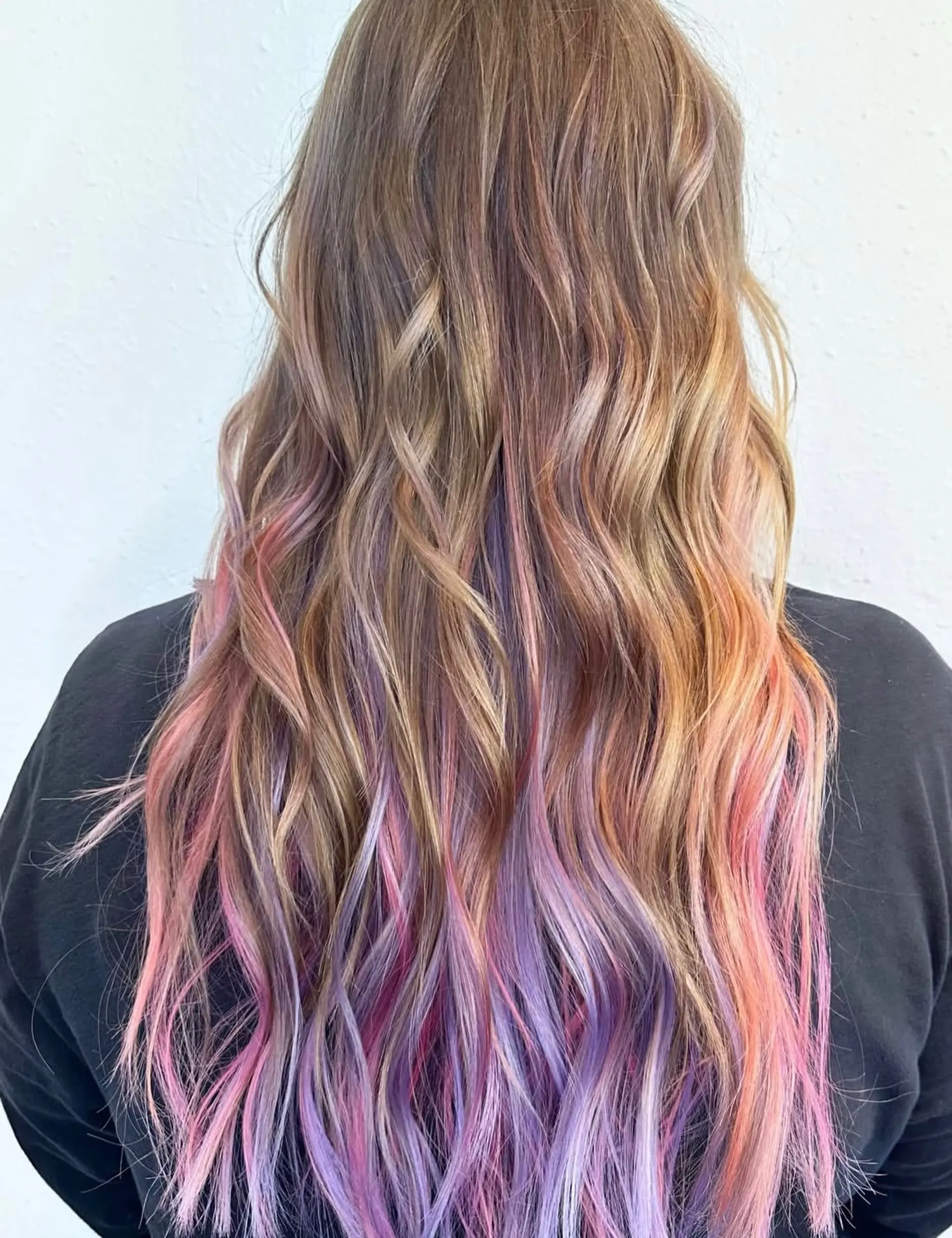 Long, tousled wavy hair featuring soft blonde and light brown base tones blended with vibrant pastel peekaboo highlights in lavender, pink, and peach. 1