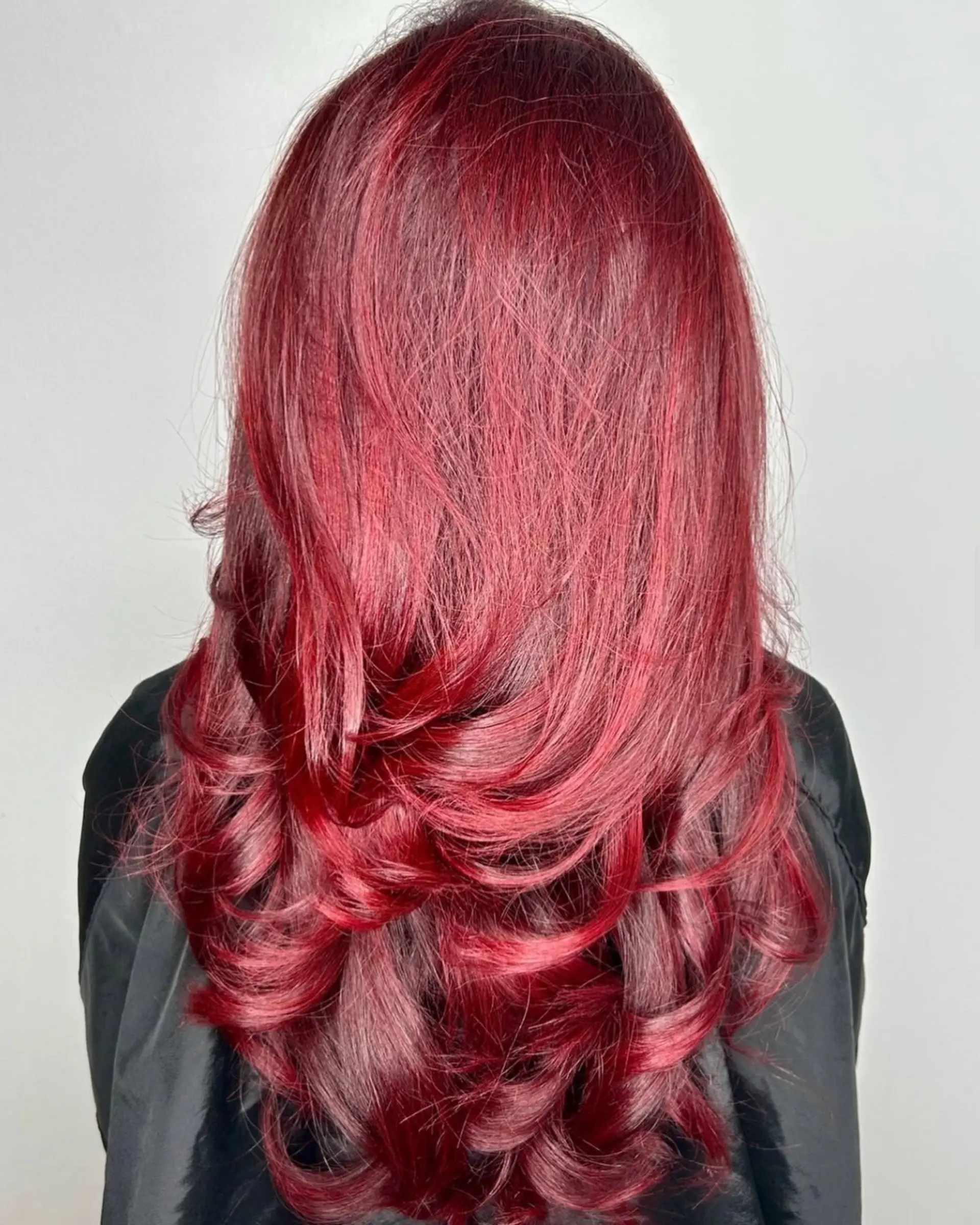 Vibrant ruby-red long hair styled with cascading layers and polished curled ends. 1