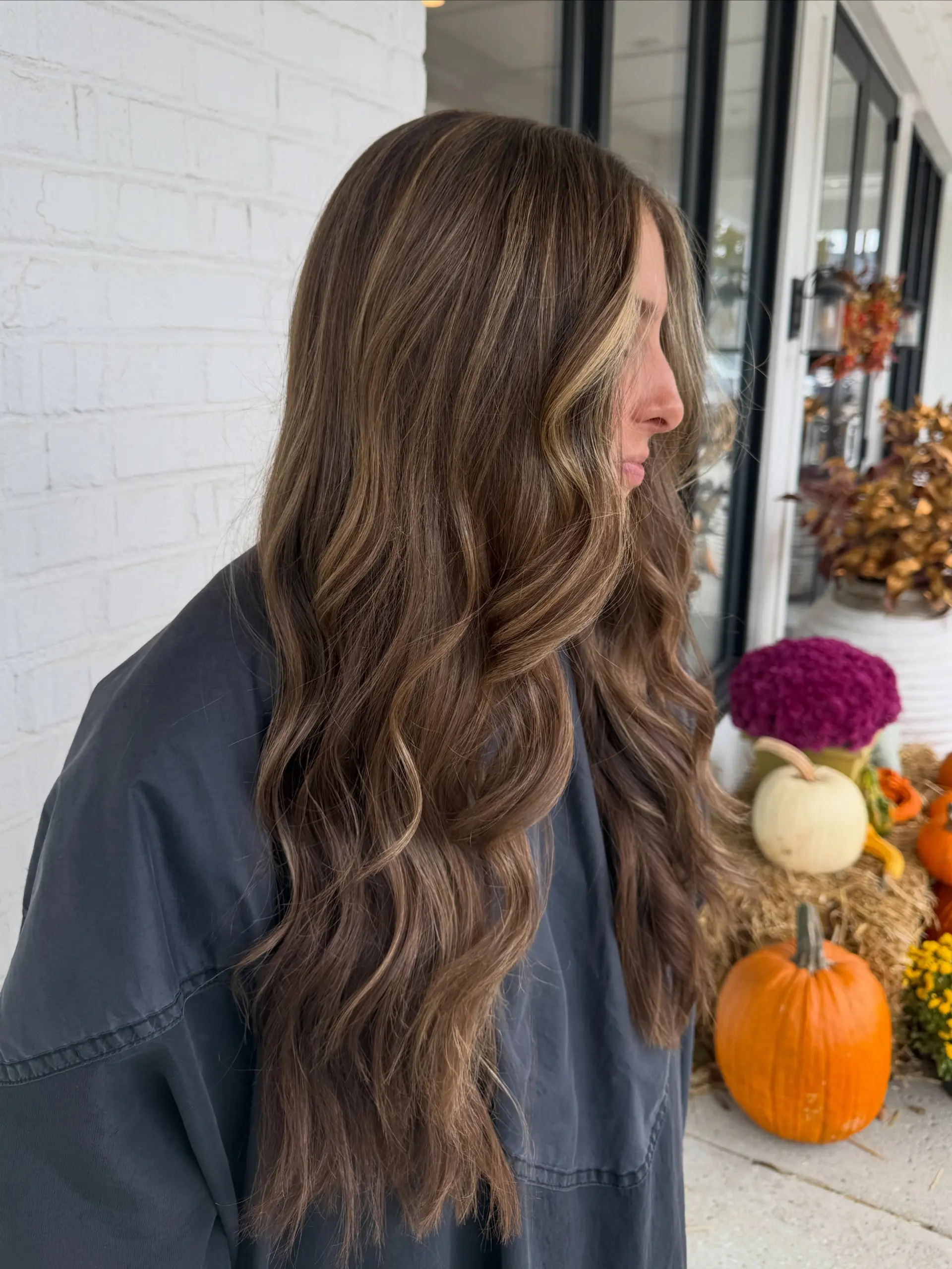 Long dimensional brunette hair styled in loose, cascading waves with subtle face-framing lighter highlights. 1
