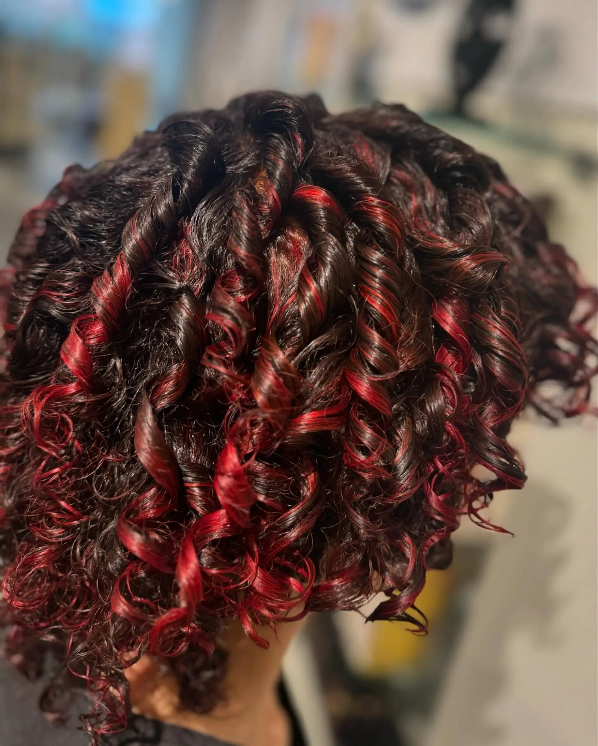A close-up view of short, glossy dark curls accented with vibrant red dimensional highlights and styled into defined ringlets. 1