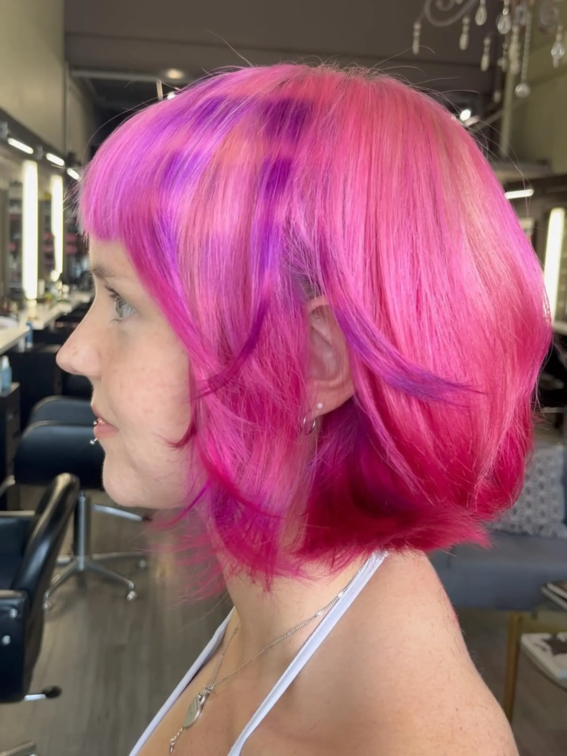 A short, textured layered bob featuring straight-across micro bangs and vivid hot pink hair with subtle purple accent panels. 1