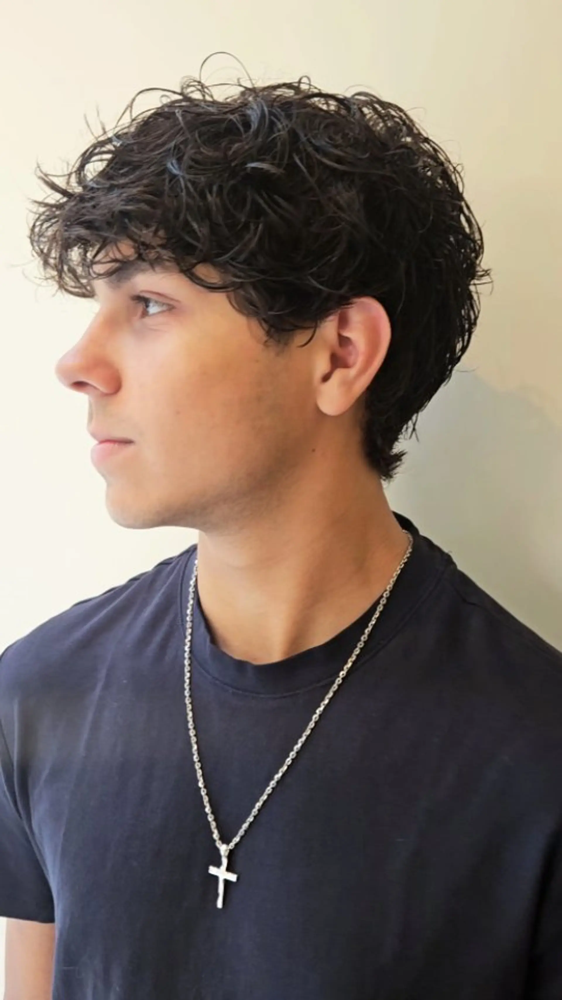 A textured short men's haircut accentuating natural waves and curls with lightly layered length on top and soft edges. 1