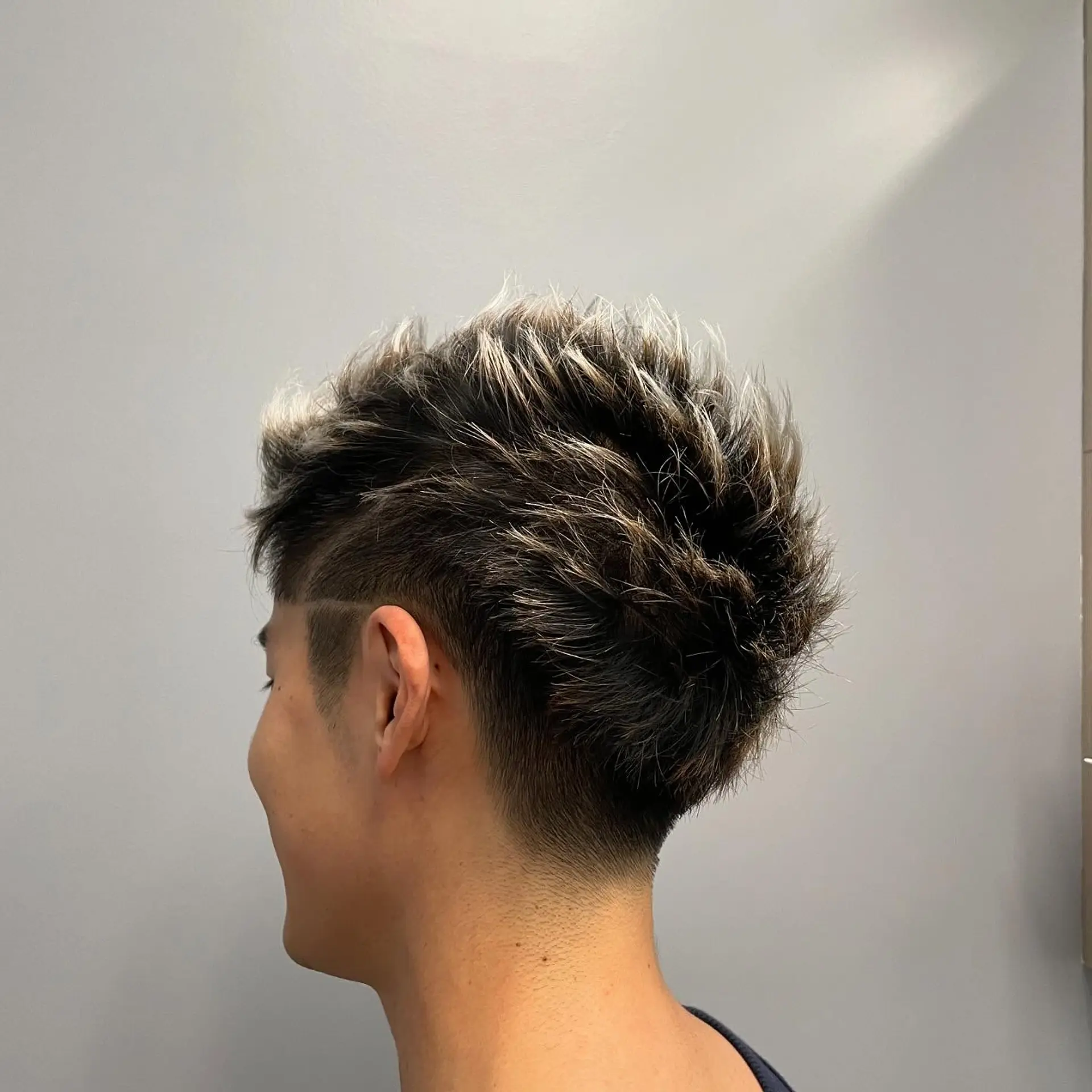 A short, spiky textured cut with a low taper fade, subtle shaved temple line, and frosted blonde tips. 1