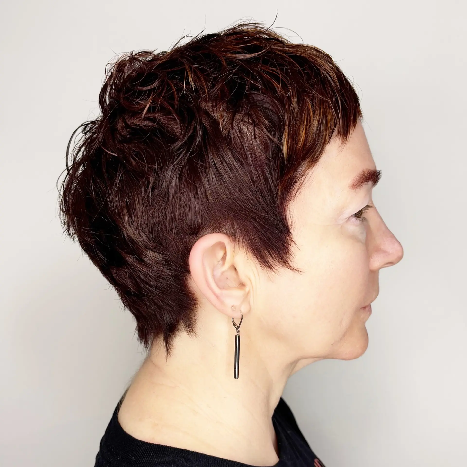 A textured, short pixie cut with soft piecey layers, micro fringe, and tapered sides in a rich dark brunette tone with warm highlights. 1