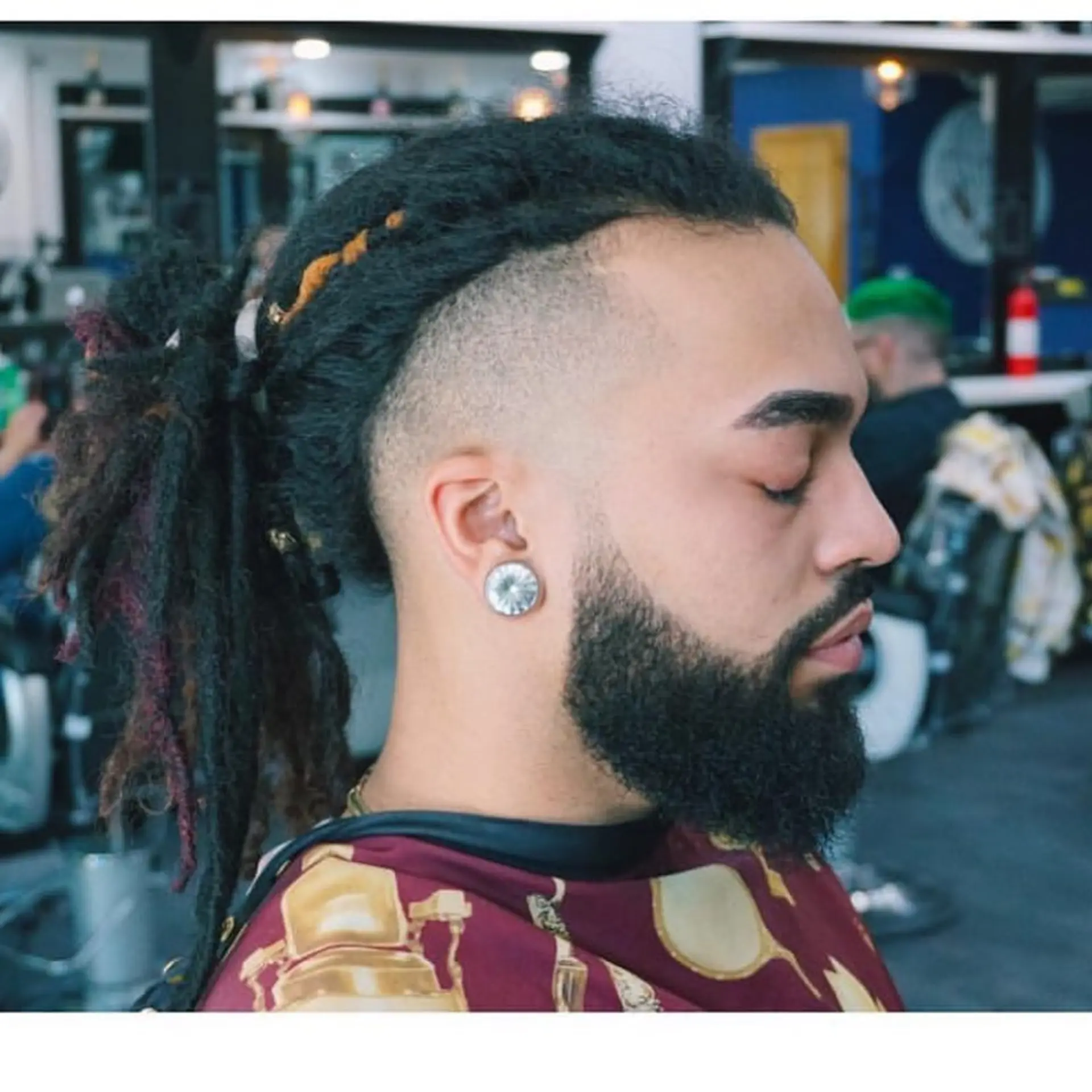 A clean high skin fade undercut paired with long locs gathered into a ponytail, accompanied by a well-groomed full beard. 1