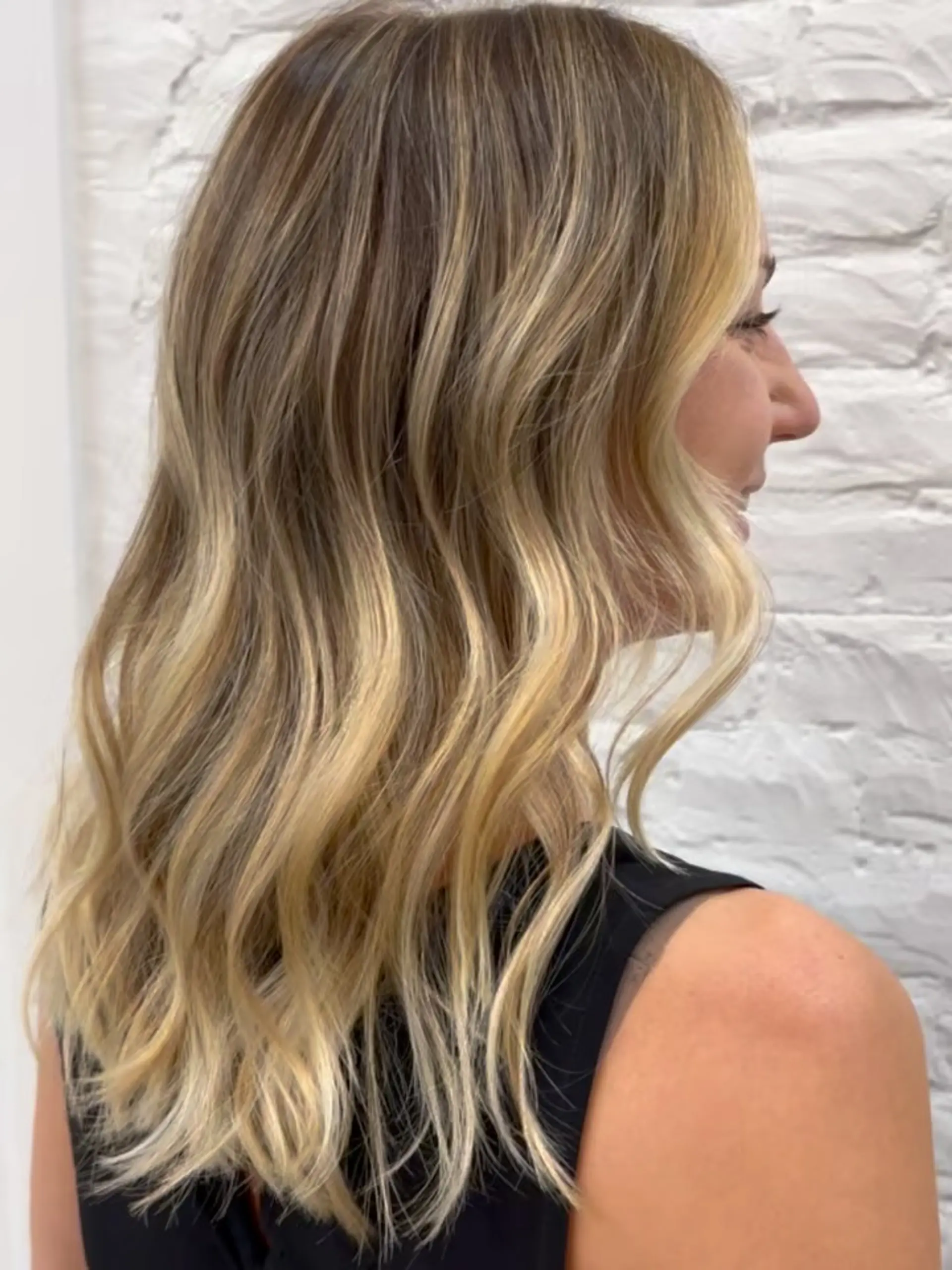 Medium-length golden blonde balayage with seamless root blending and soft, relaxed waves. 1