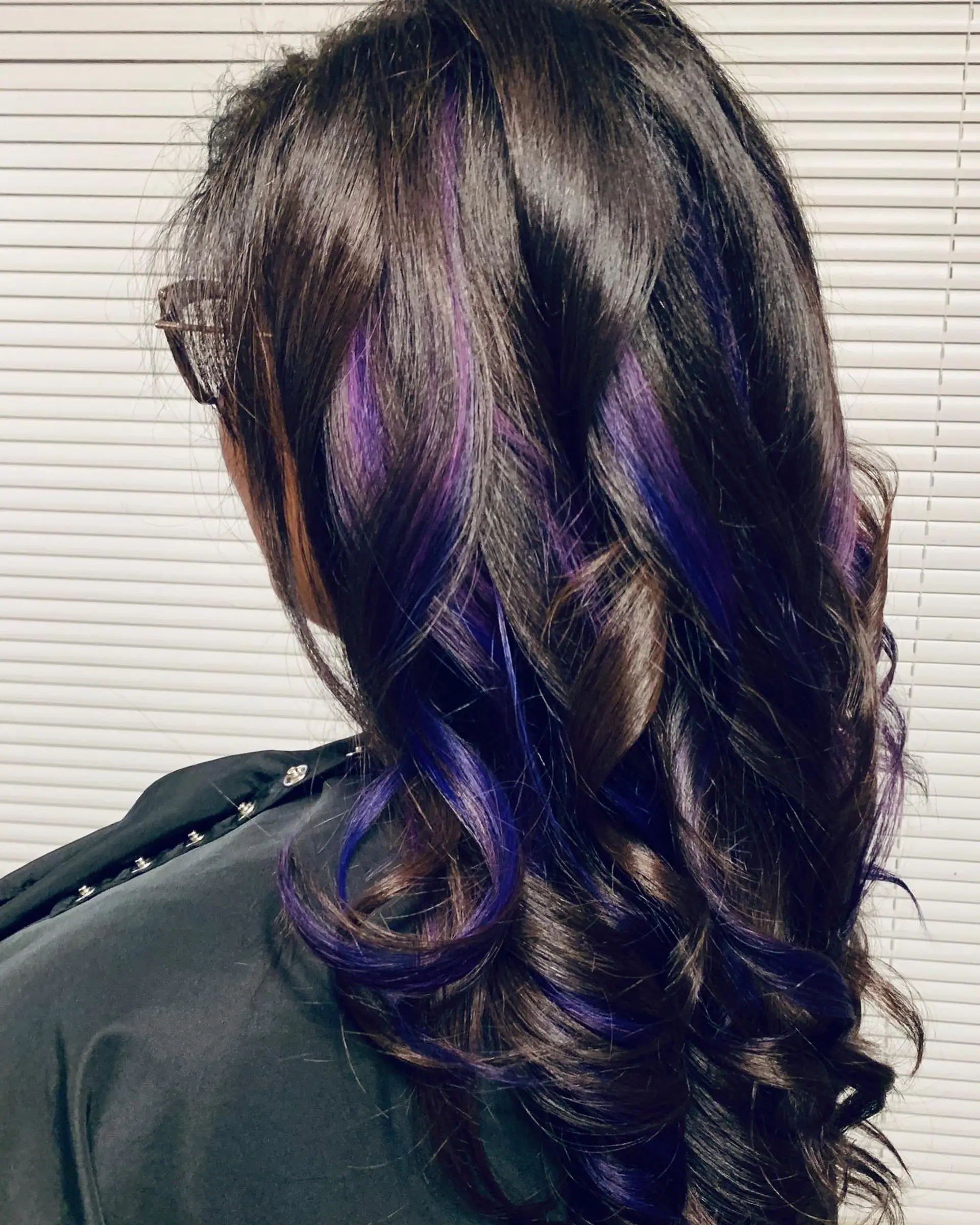 Long dark brown hair styled in defined curls featuring vibrant purple peekaboo extensions. 1