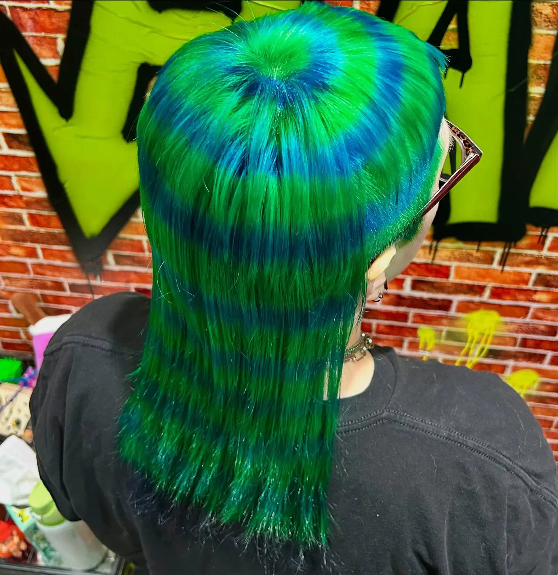 A hypnotic concentric circle pattern dyed in alternating rings of vibrant green and electric blue across straight hair styled into a mullet. 1