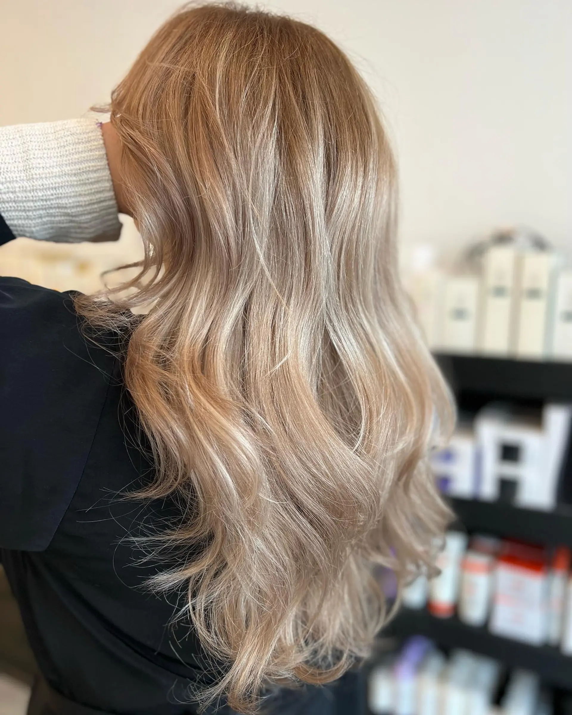 Long dimensional ash blonde hair styled in soft, cascading waves with a natural root shadow. 1