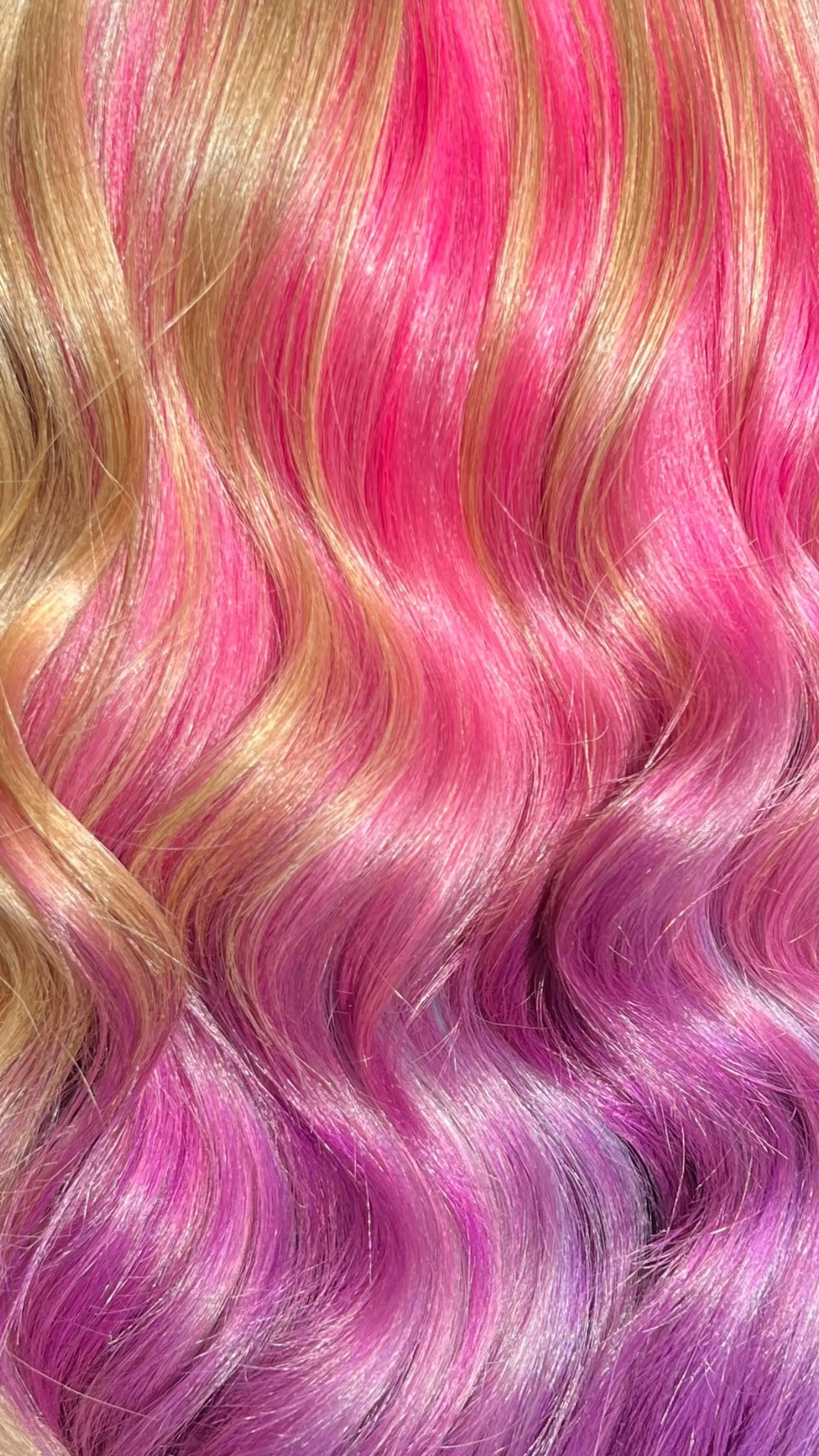 Glossy wavy hair featuring vivid hot pink ribbons blended through golden blonde lengths melting into purple tips. 1