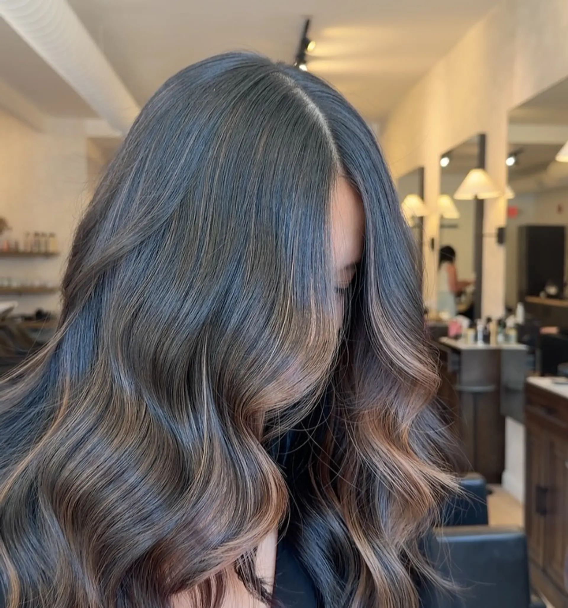 Rich dark brown hair enhanced with subtle caramel balayage highlights, styled into soft, flowing salon waves. 1