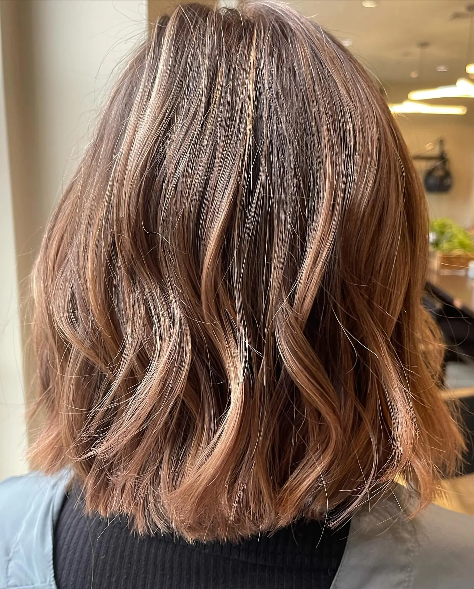 A textured shoulder-length bob styled with soft, piecey waves and warm caramel blonde dimensional highlights. 1