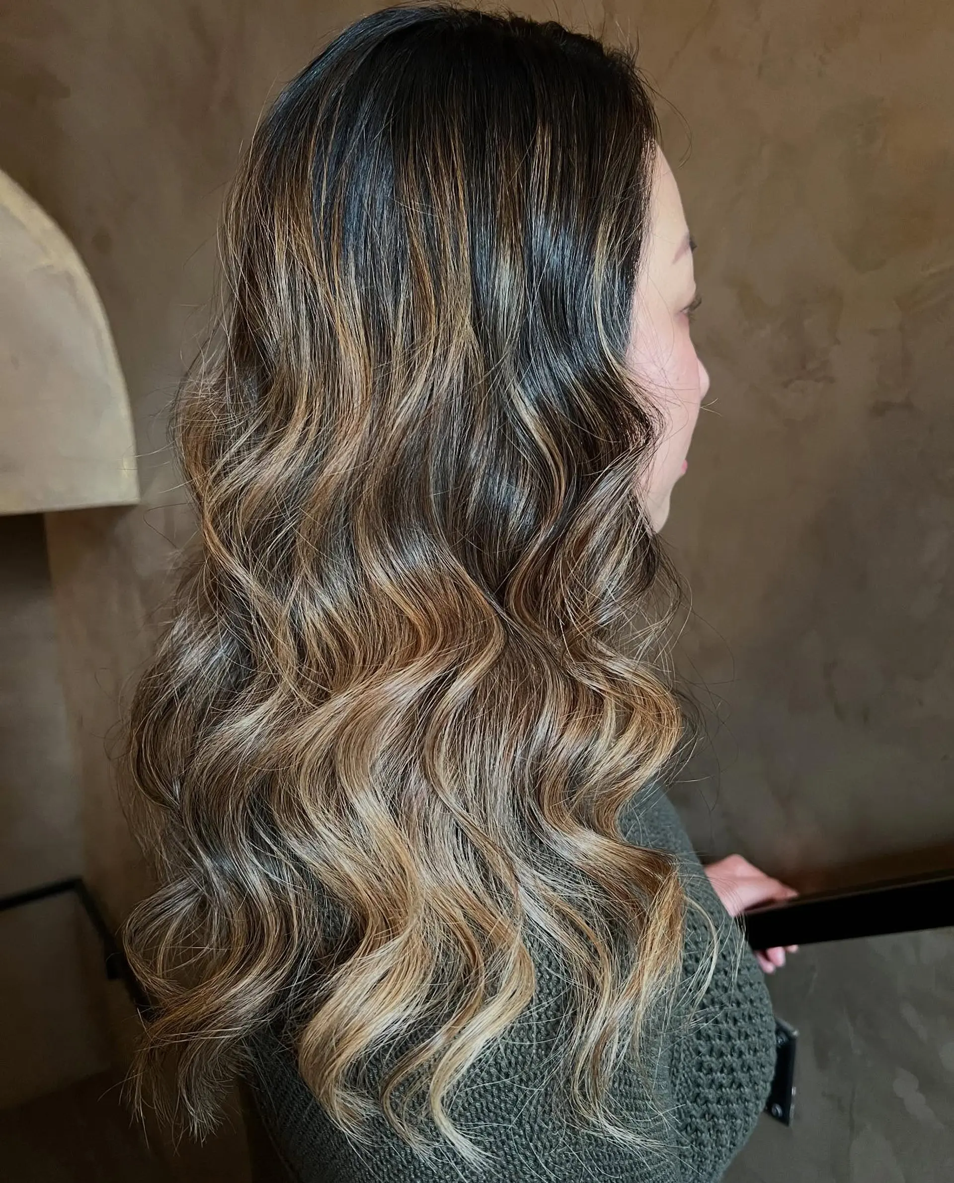 Long dark brunette hair featuring seamless caramel and honey balayage highlights, styled in polished, glossy waves. 1