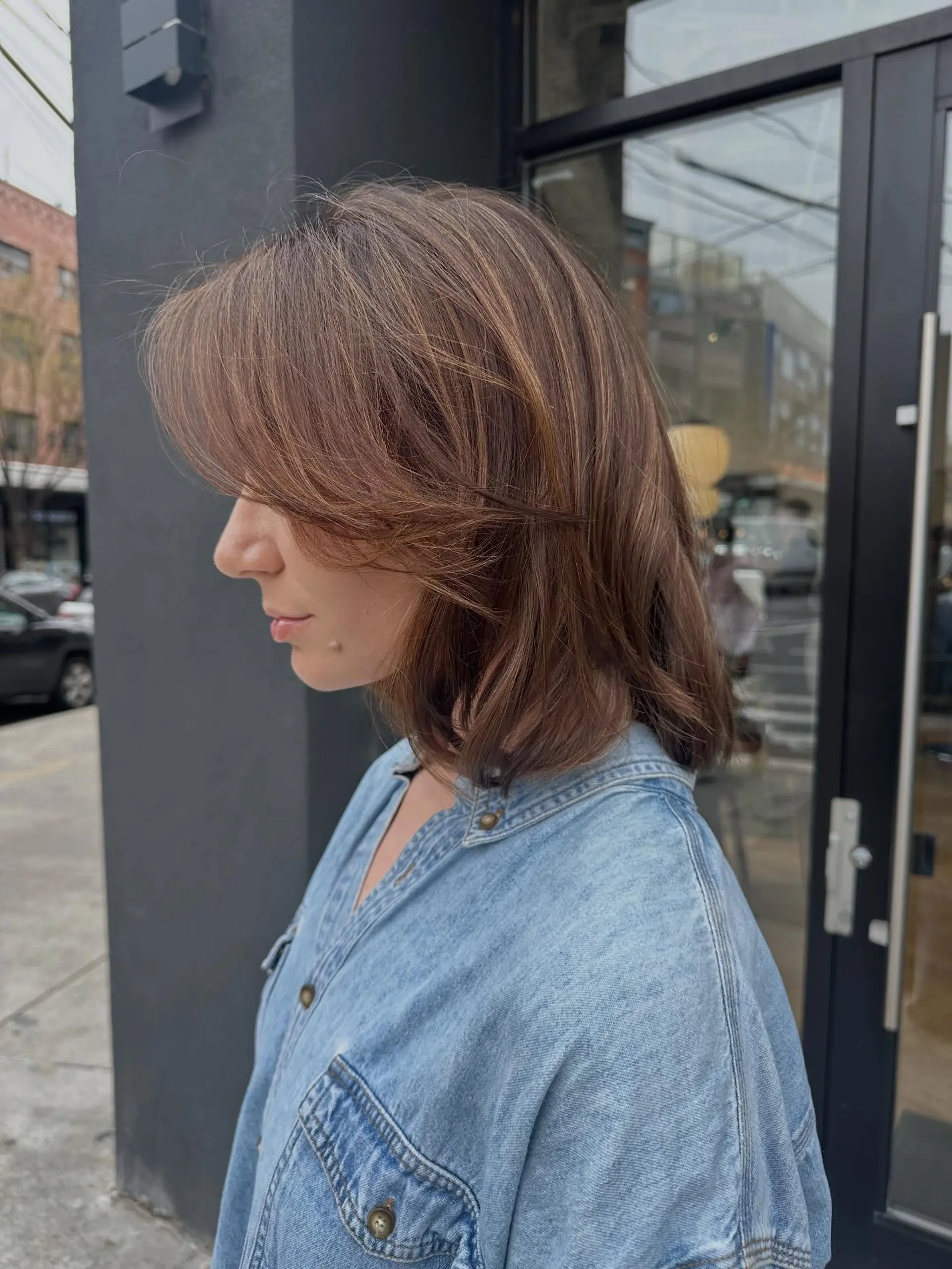 Shoulder-length layered bob with face-framing curtain bangs and subtle warm highlights. 1