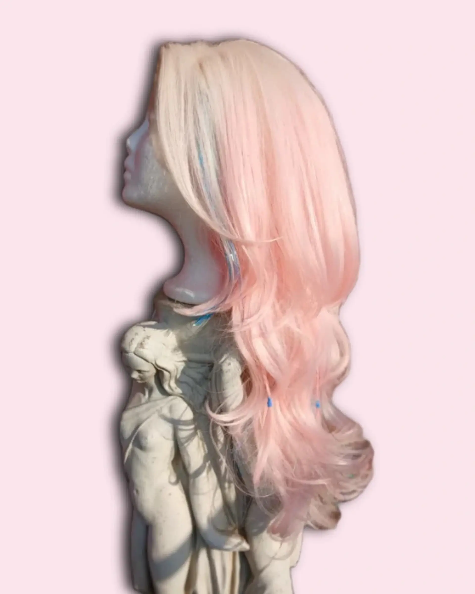 A long pastel pink styled wig with soft wavy layers and subtle blue accent strands. 1