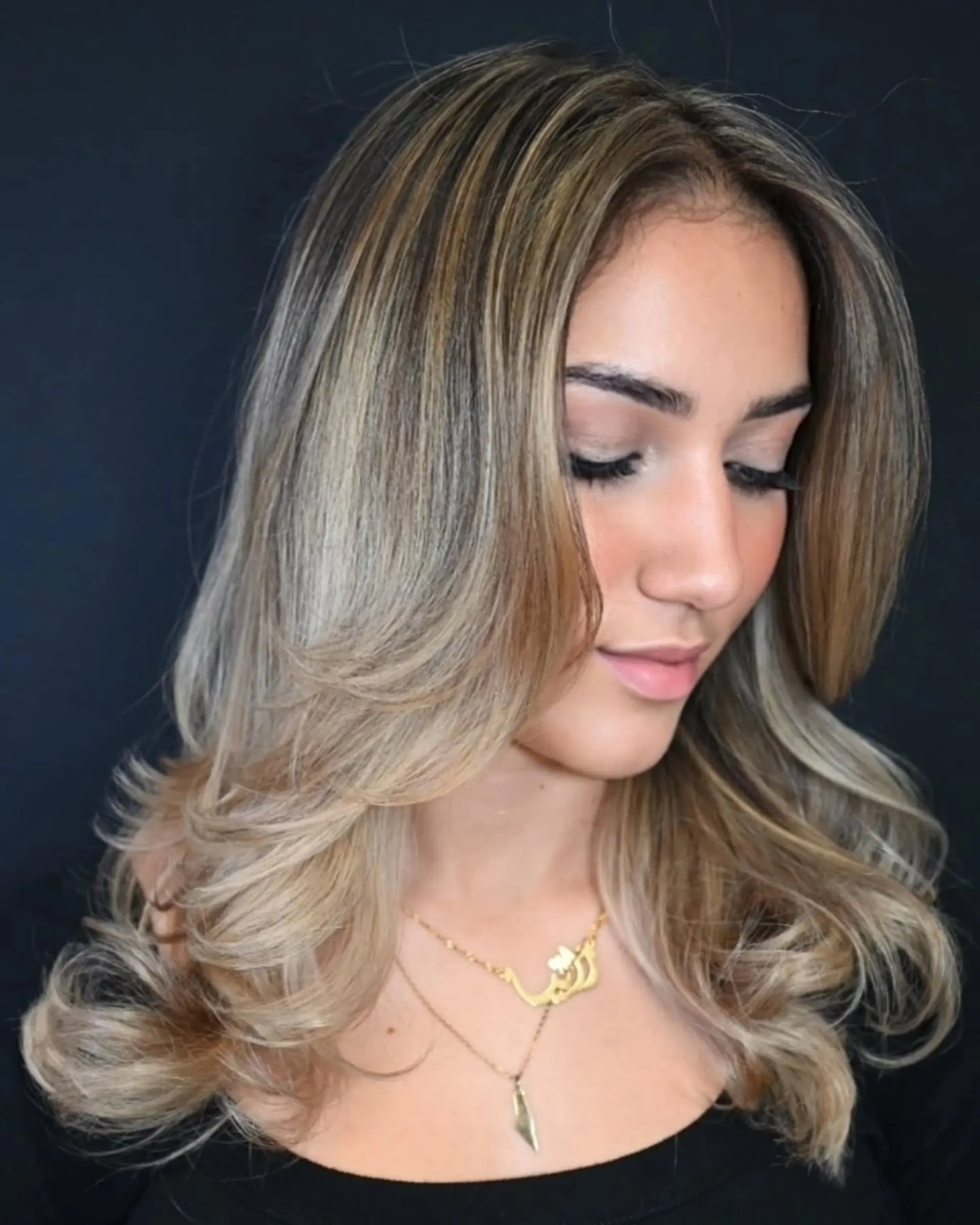Long layered ash blonde hair styled with bouncy, outward-curled ends and face-framing curtain layers. 1