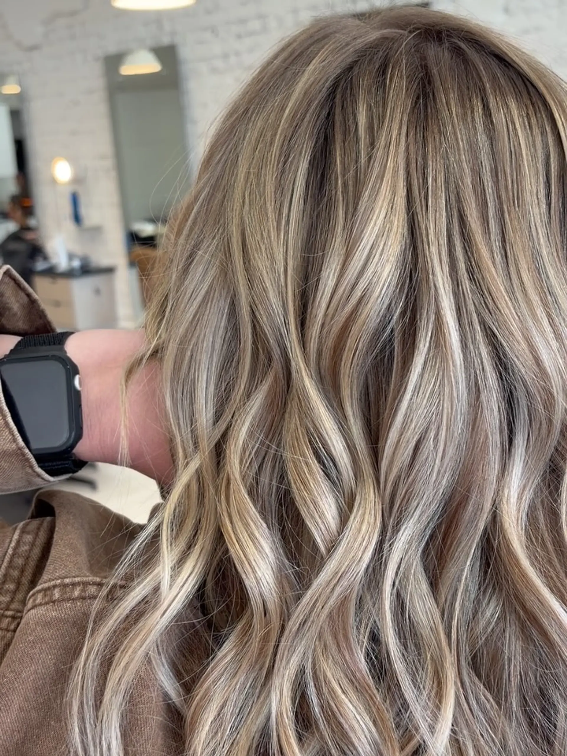 Dimensional beige and ash blonde highlights seamlessly blended into a light brown base and styled with soft waves. 1