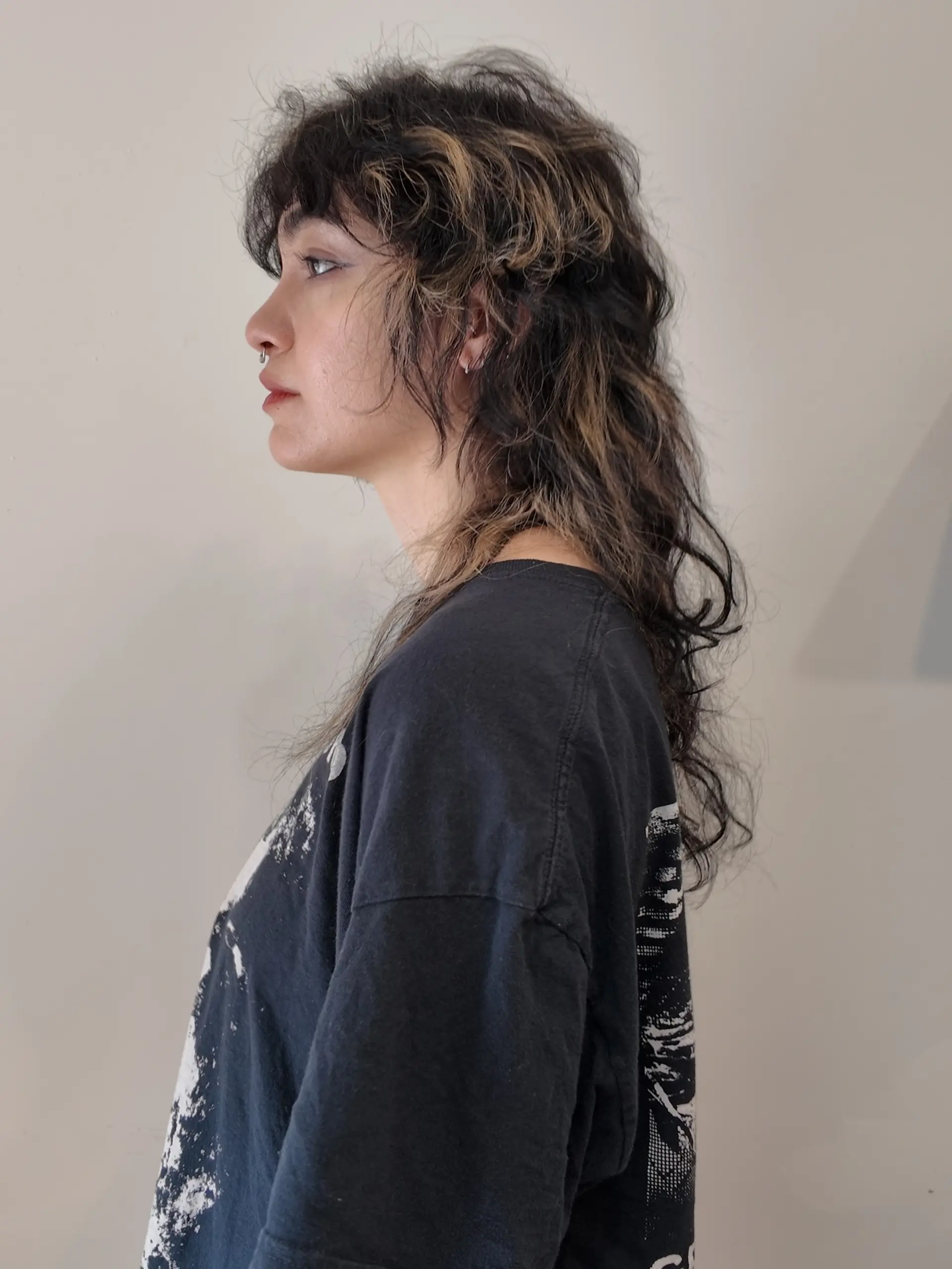 A textured shag mullet with full fringe bangs and contrasting chunky warm blonde highlights on dark wavy hair. 1