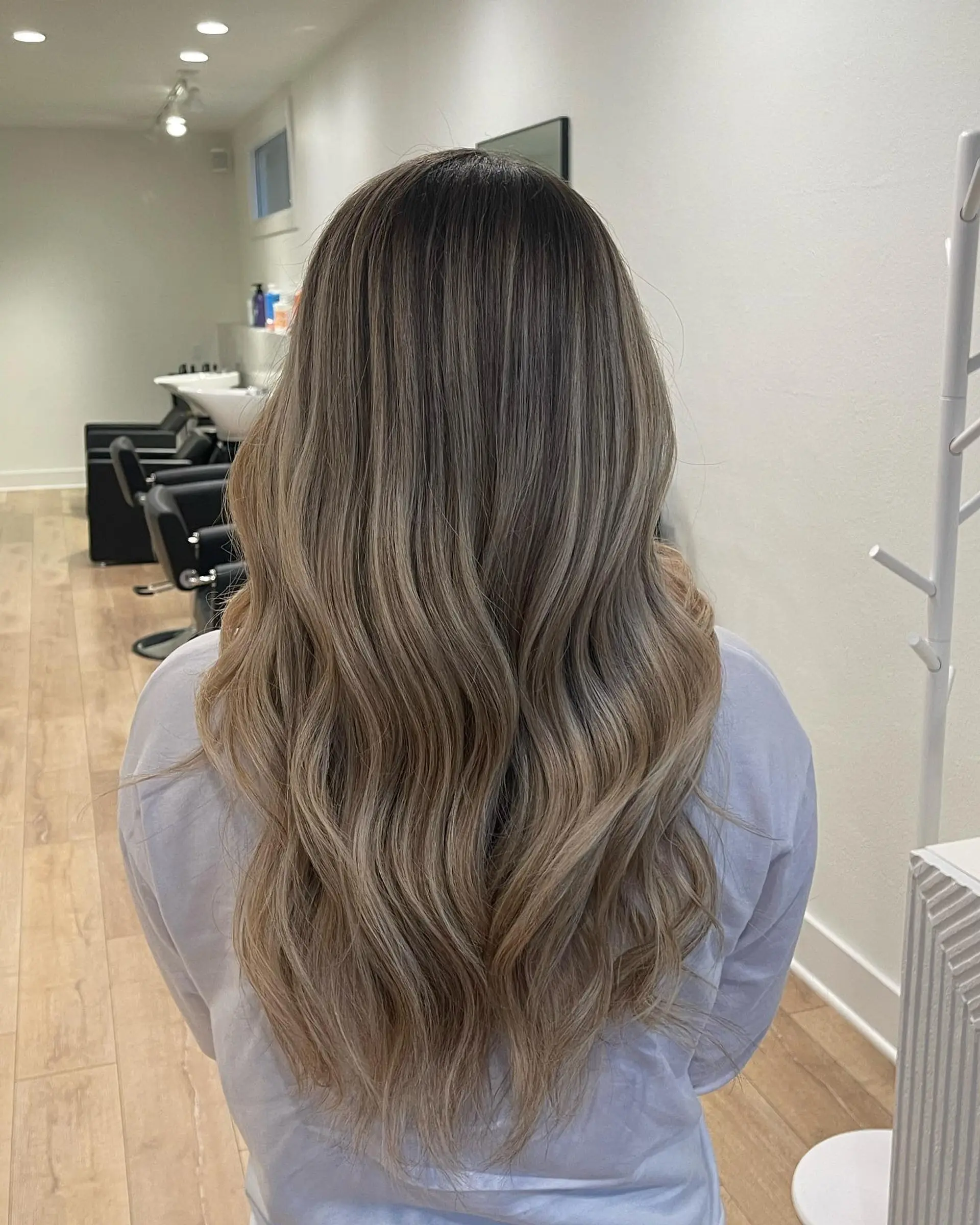 Long cascading waves featuring a seamless cool-toned ash blonde balayage with a blended shadow root. 1