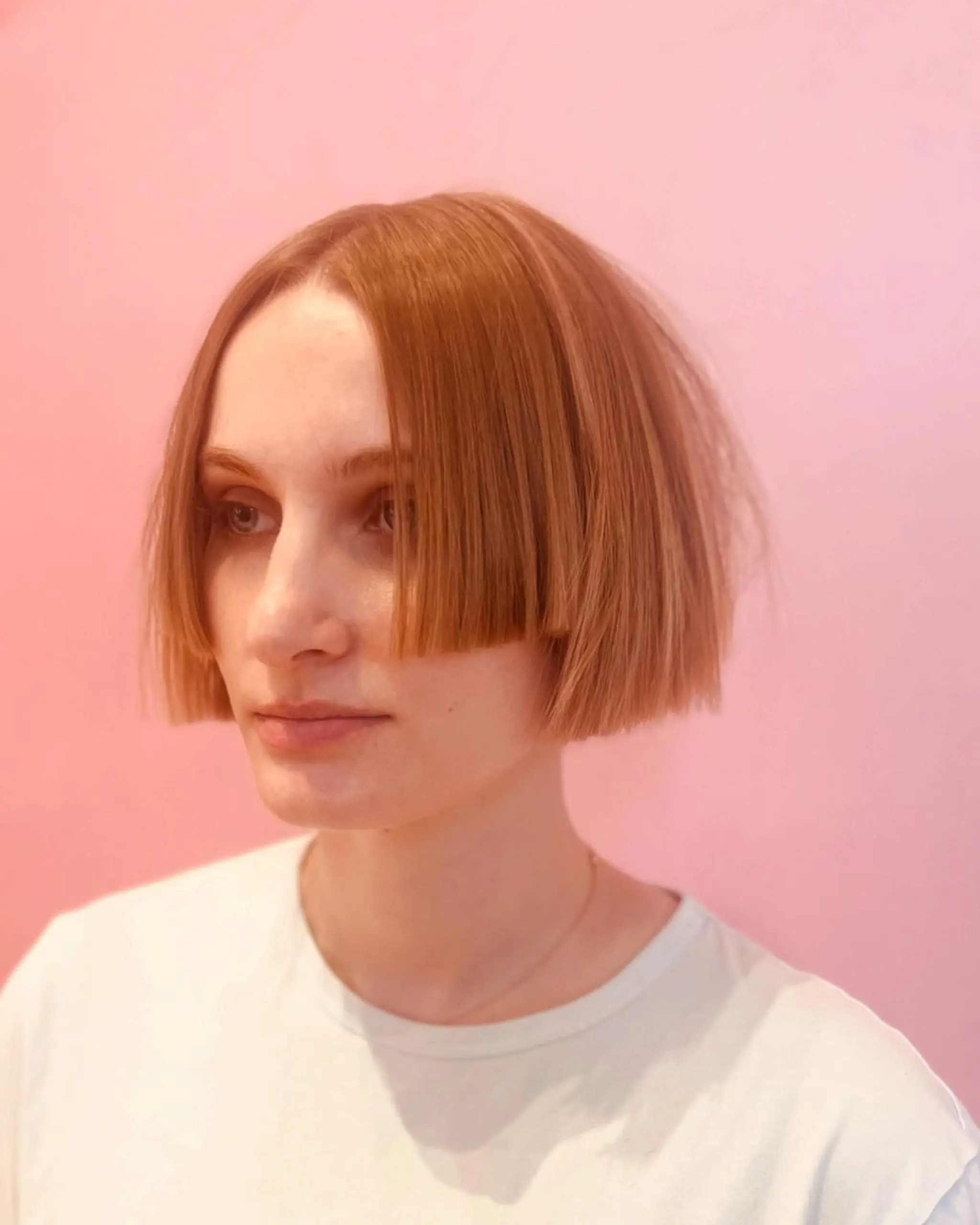 A Chic Angular Bob with straight, light brown hair cut to a short length. The style showcases a blunt cut with a symmetrical, angular design that frames the face neatly.