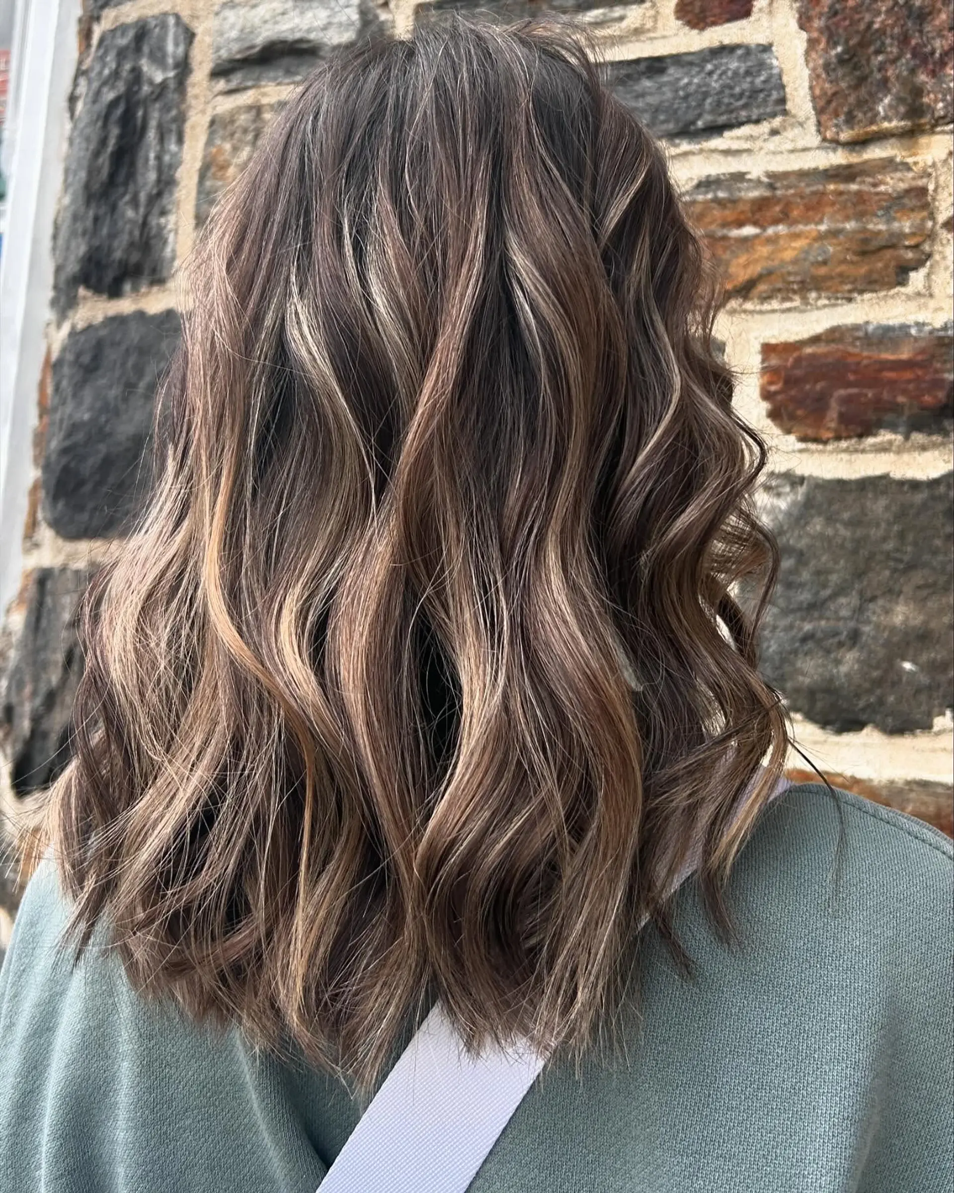 Medium-length textured lob featuring multidimensional blonde and brunette balayage styled with relaxed waves. 1