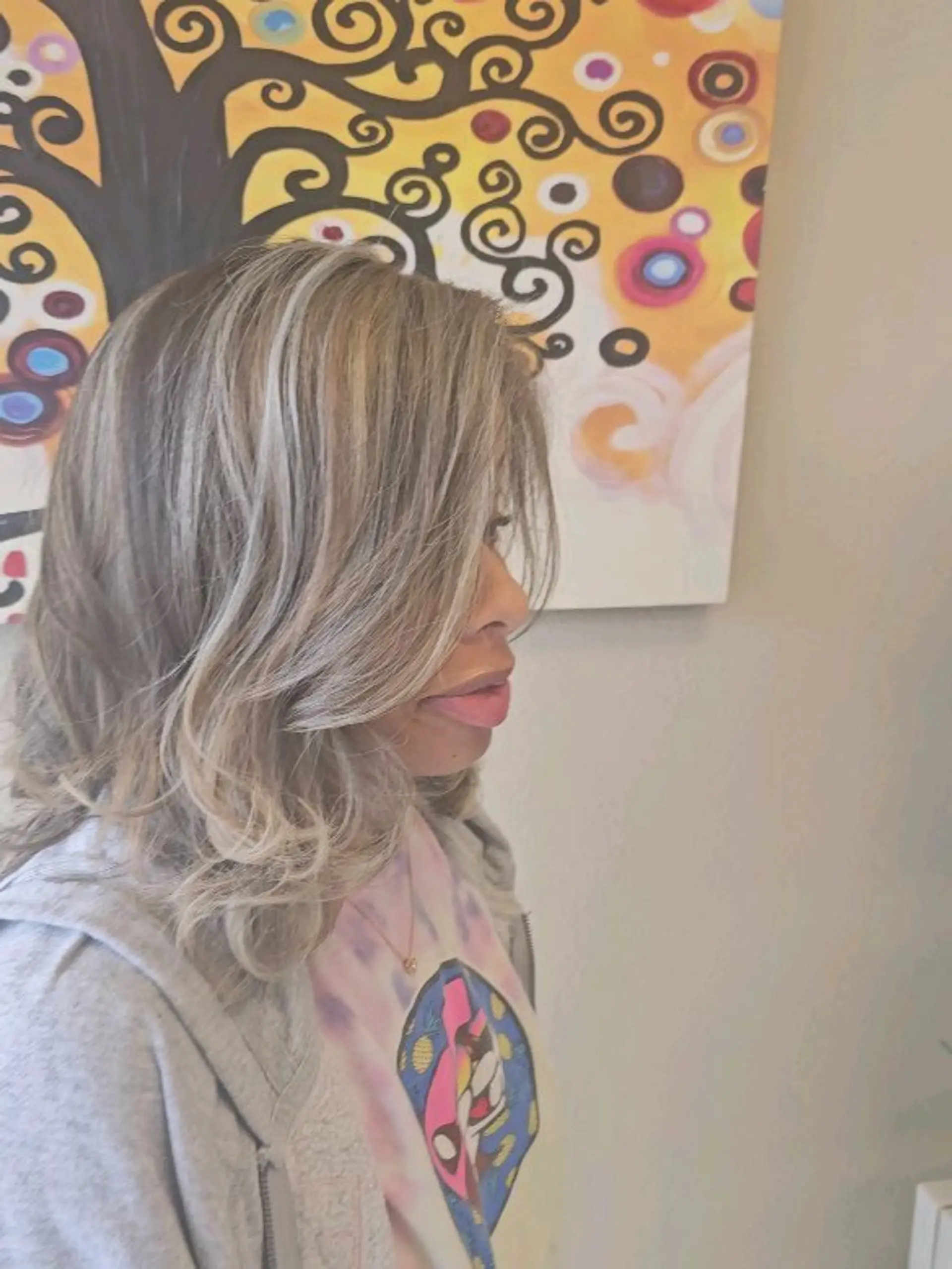 Medium-length layered hairstyle styled in soft waves with side-swept bangs, featuring cool-toned ash blonde highlights blended throughout. 1